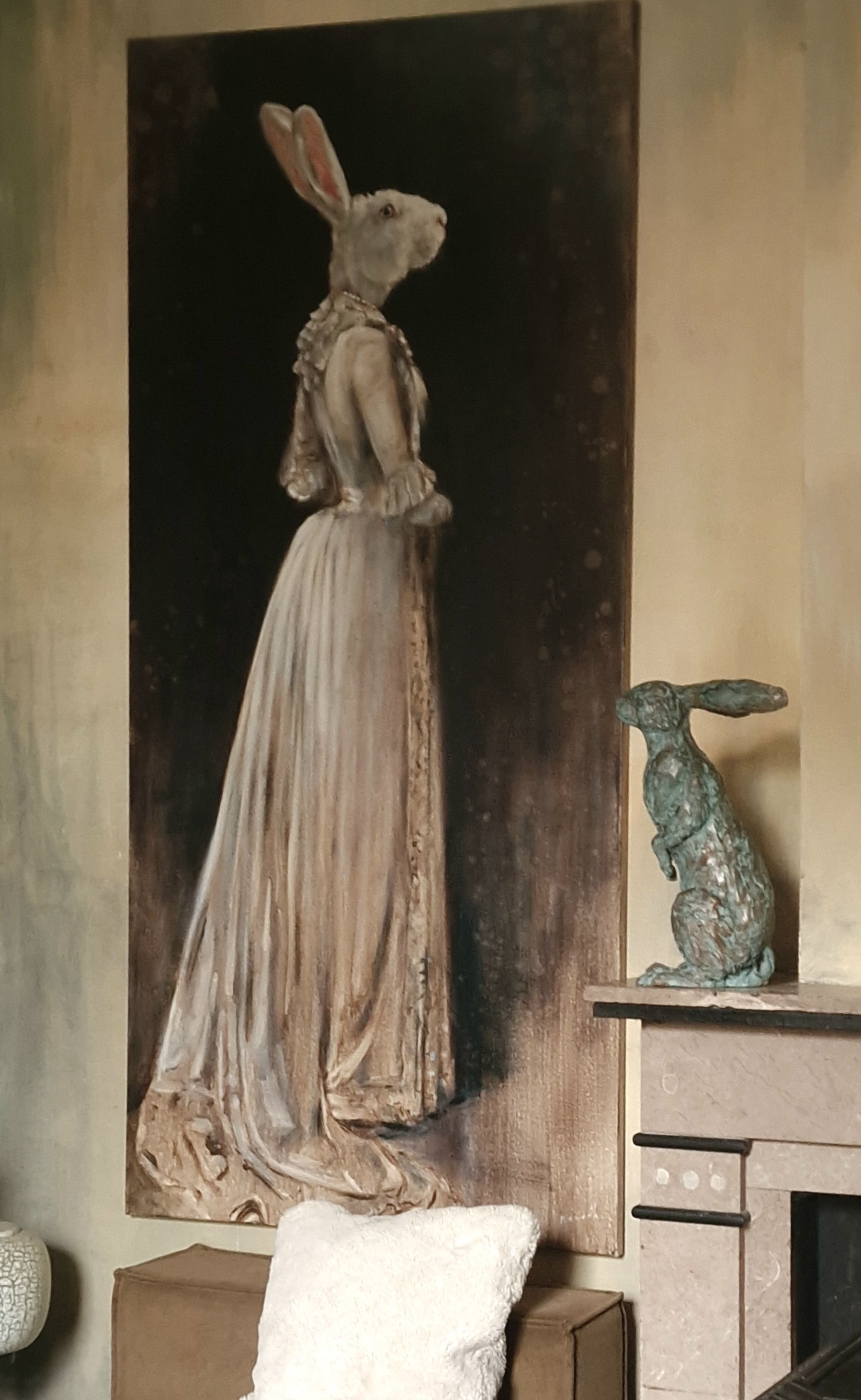Een hoge beige sculptuur van een figuur met een hazenkop staat naast een open haard in een schemerige kamer.