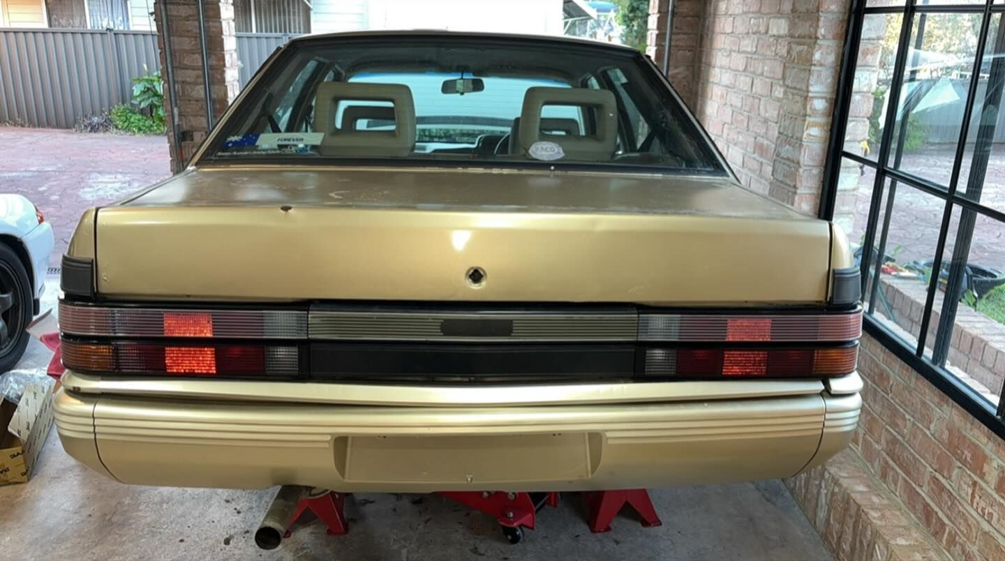 Rear View of a Gold Vintage Sedan Car on Jack Stands Inside a Garage — Amrix Automotive In Bankstown, NSW