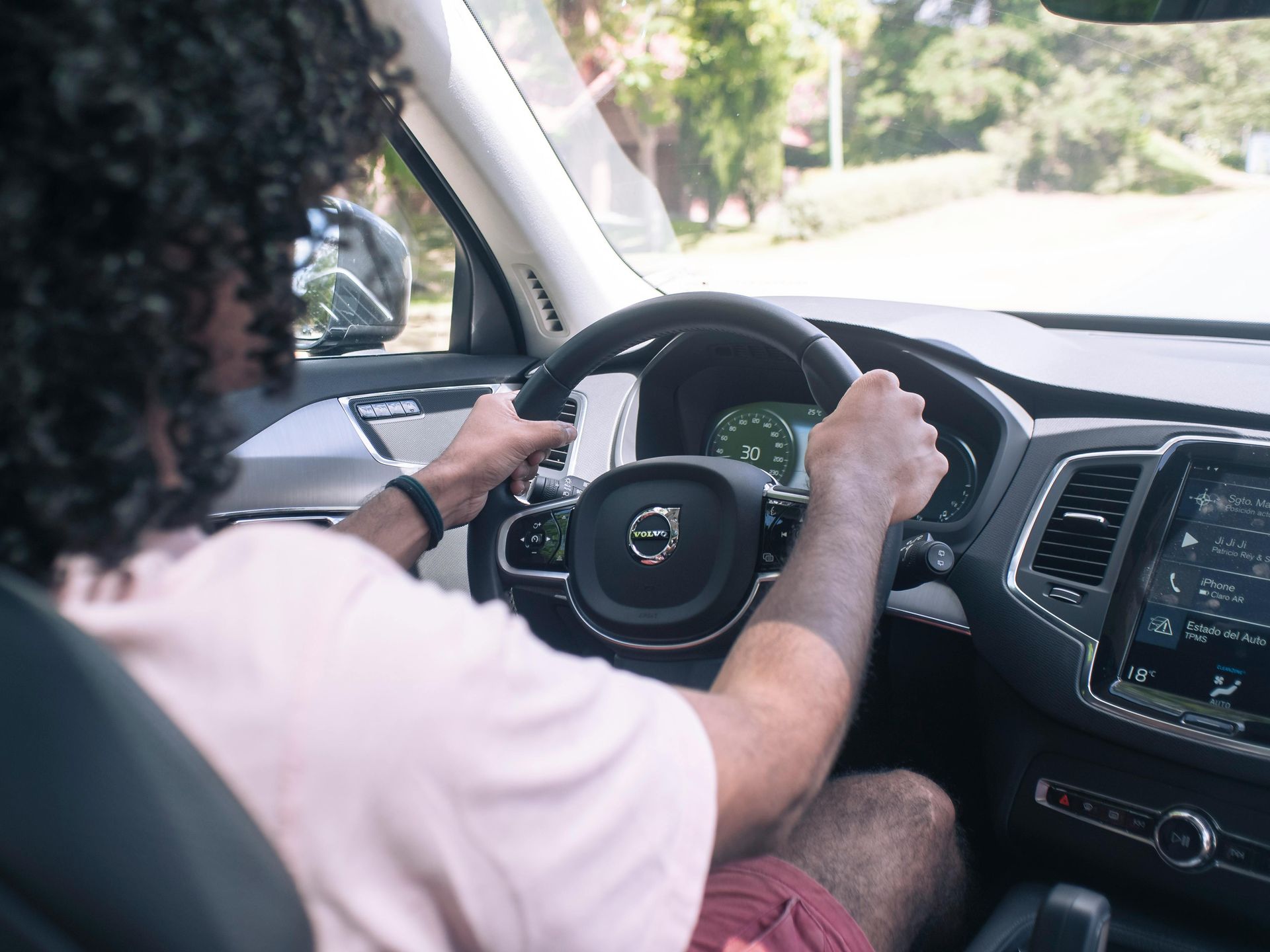 Person with curly hair driving a Volvo, holding the steering wheel. Interior view of the car with dashboard visible — Amrix Automotive In Sefton, NSW