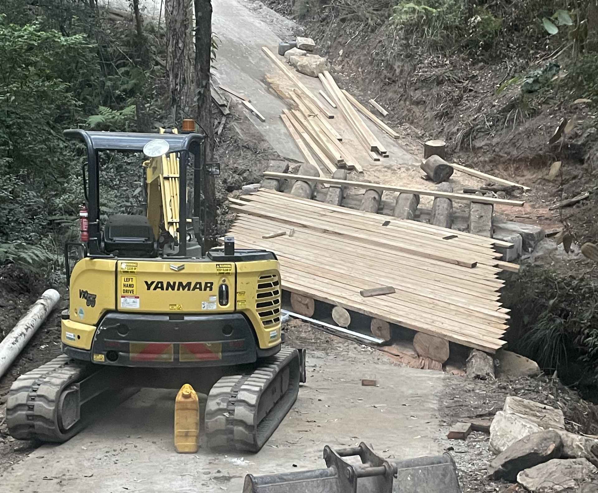 Yellow excavator with a pile of timber.