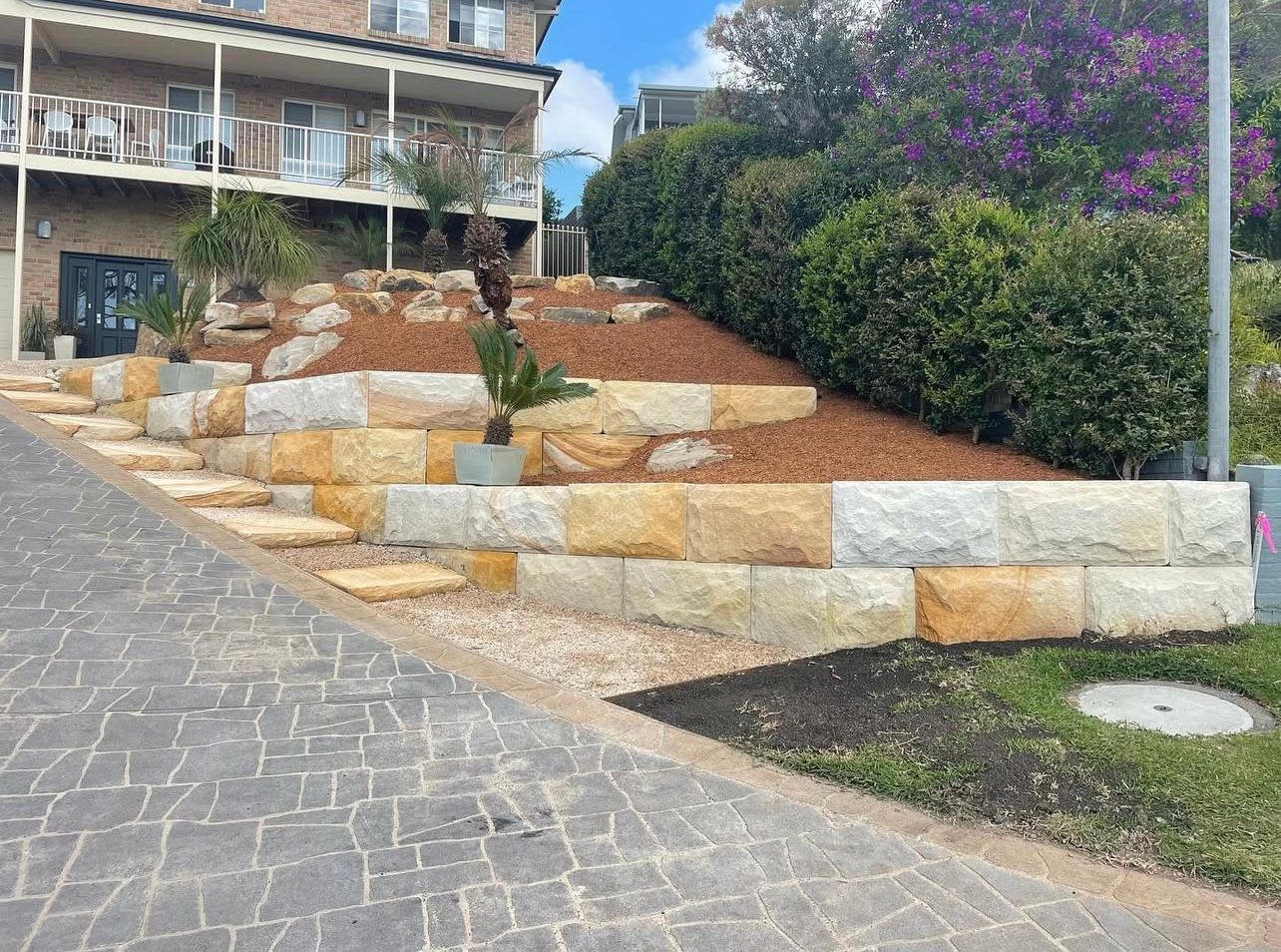 Stone steps and retaining walls lead up a hillside, with greenery and building in the background.