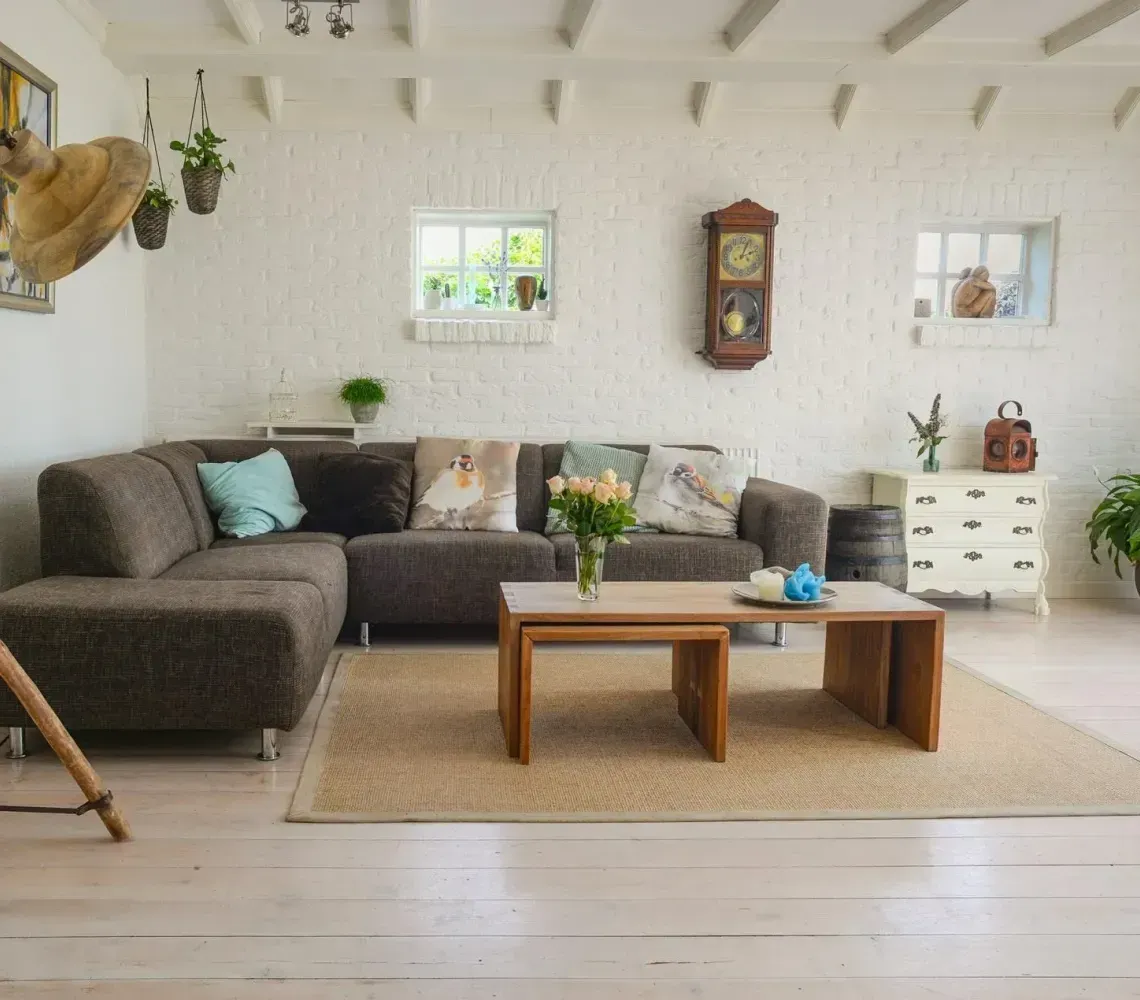 A cozy living room with a brown sectional sofa, two wooden coffee tables, a neutral rug, and a brick wall.