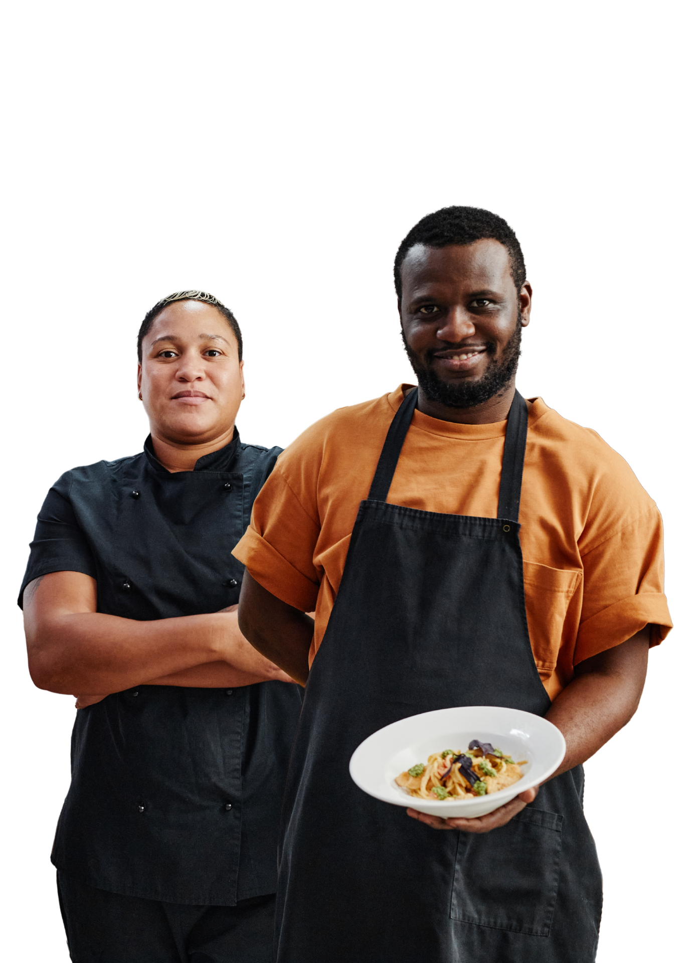 Two chefs, one holding pasta, smiling, the other with arms crossed, smiling, in a kitchen.