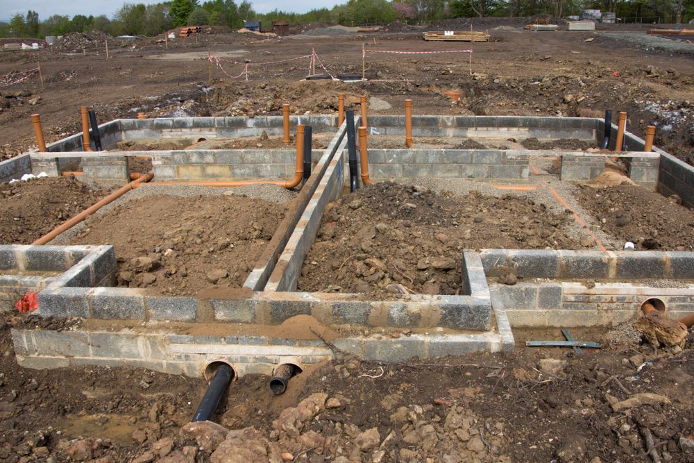 Concrete foundation footings and pipes at a construction site with dirt and wooden stakes