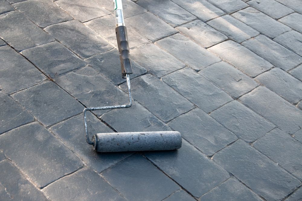 Roofing roller on a gray shingle roof applying sealant near a seam