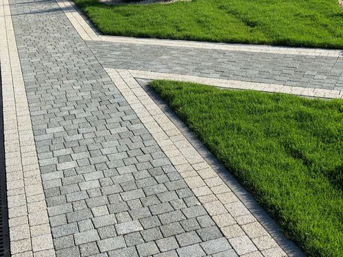 Gray stone walkway beside bright green grass, forming clean diagonal lines in a landscaped area