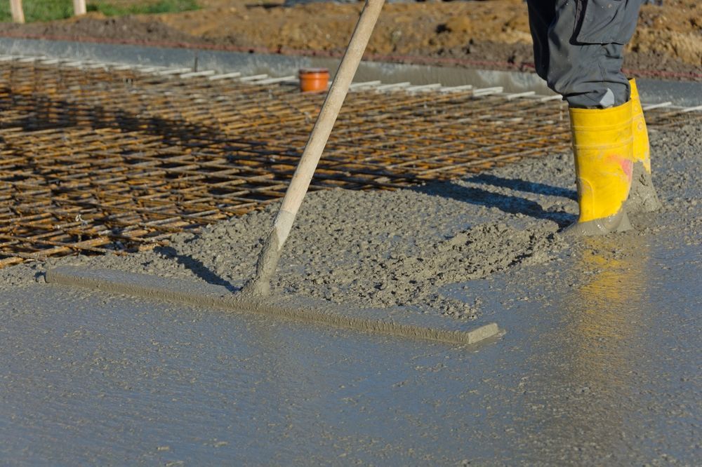 Concrete being spread over rebar at a construction site, with a worker’s yellow boots visible.