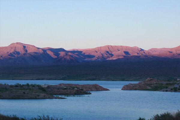 Sunlit pink mountains beyond a blue lake at dusk