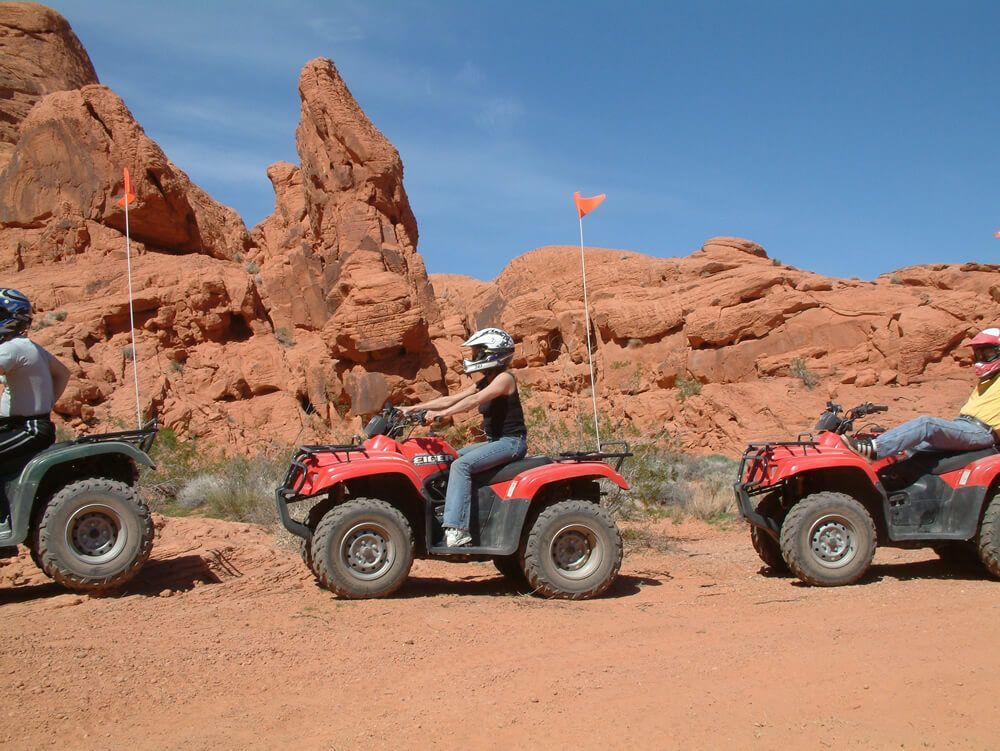 ATVs with riders on a dirt trail in a red rock desert landscape