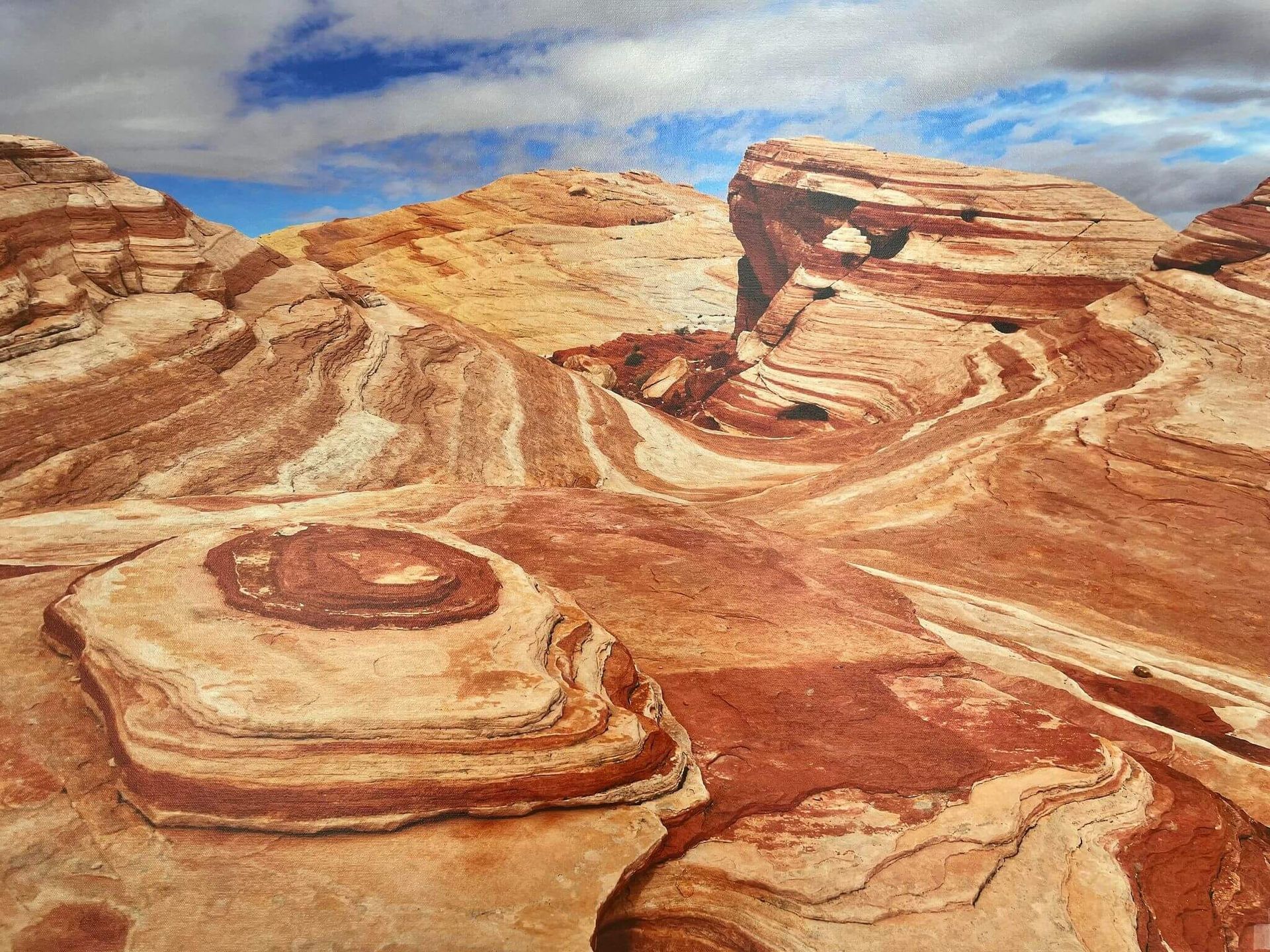 Layered sandstone rock formations in a red desert under a partly cloudy blue sky