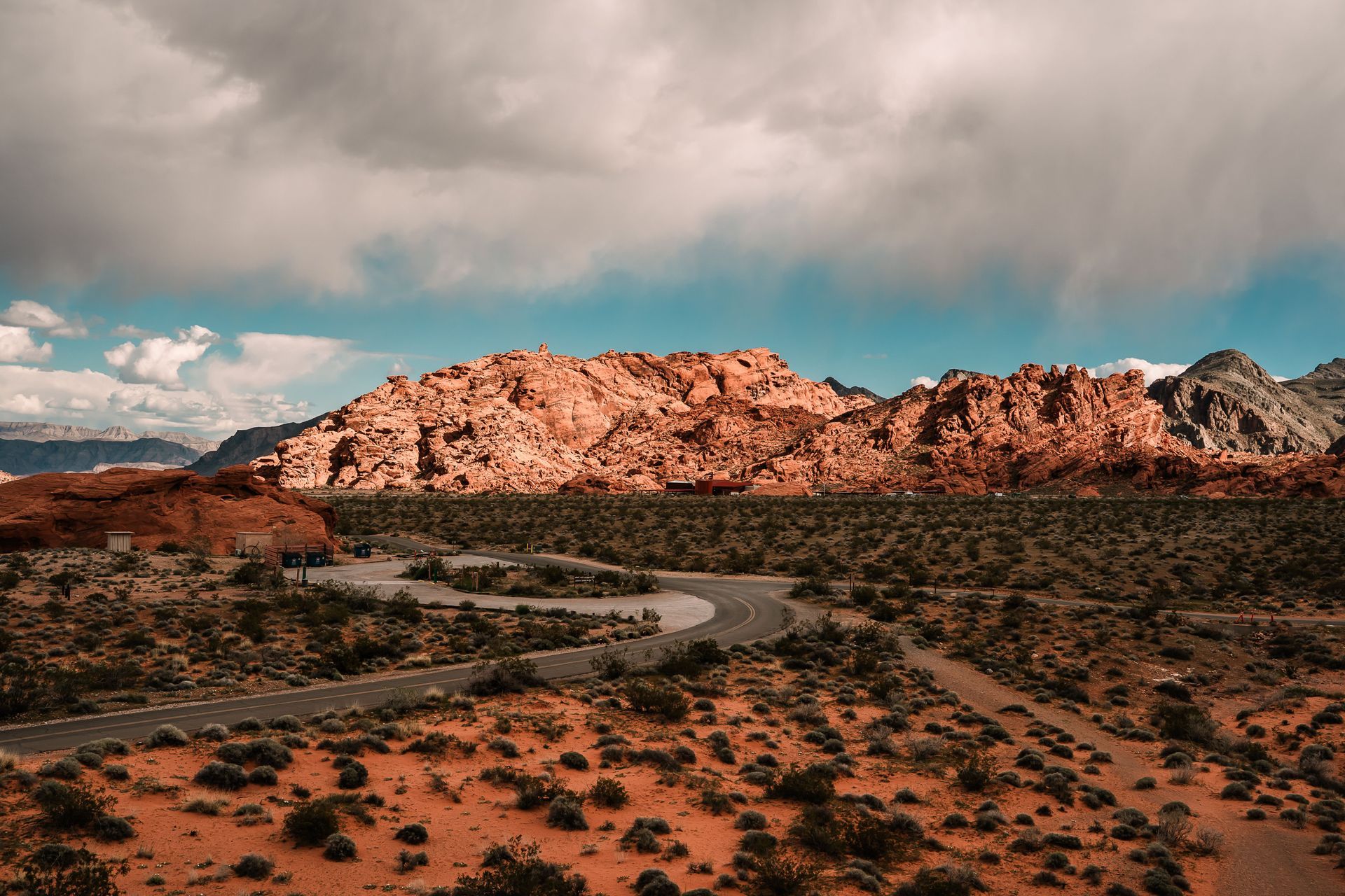 Red rock desert hills under dramatic cloudy sky with a winding dirt road