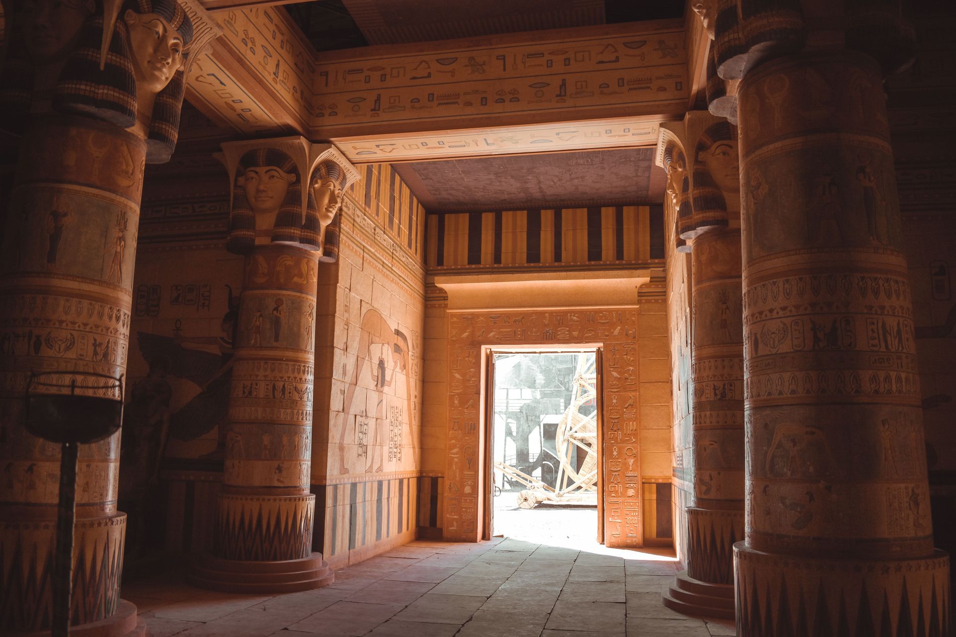 Ancient sandstone temple hall with carved columns and a bright doorway opening to sunlight outside