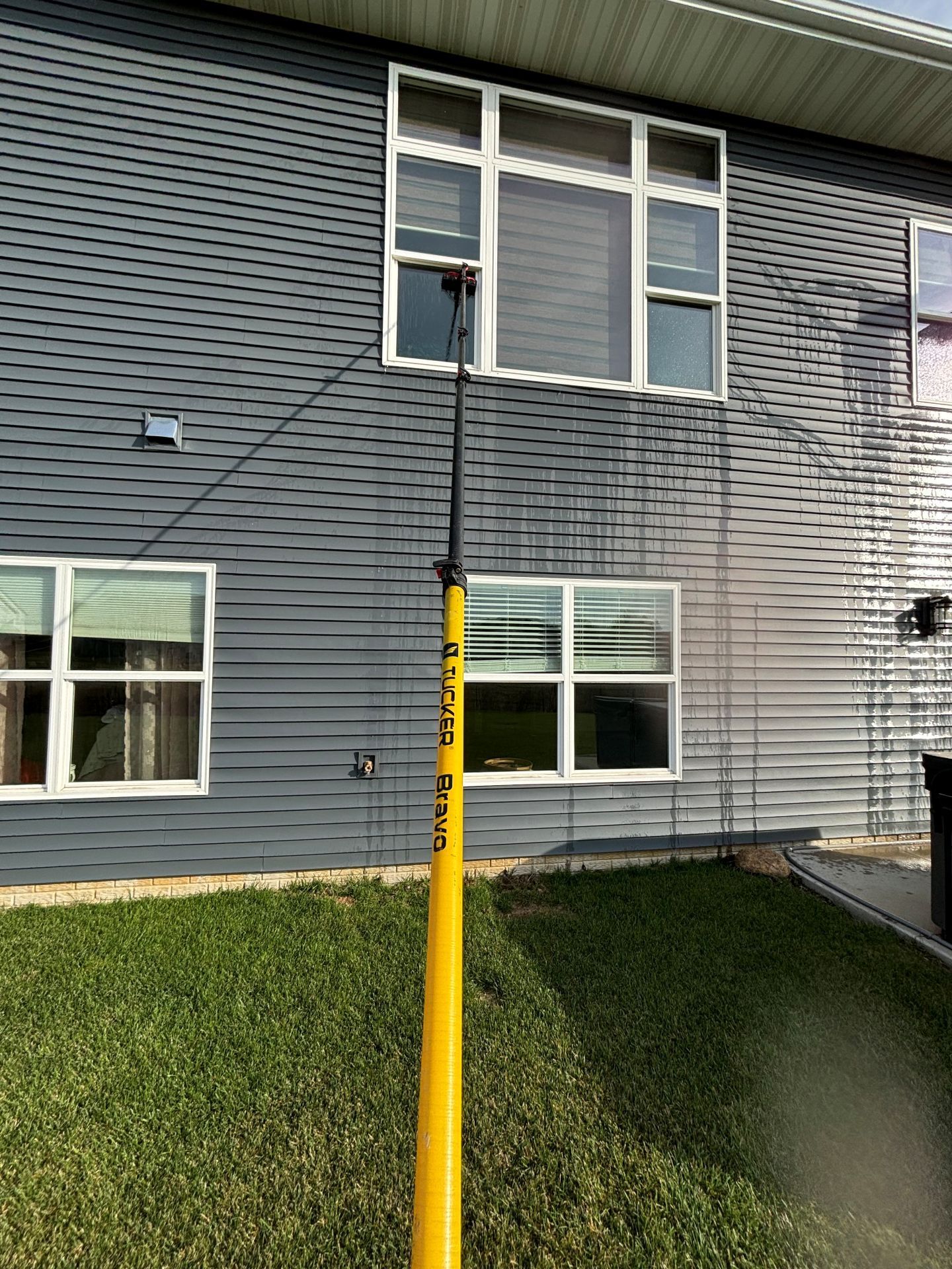Yellow pole reaching to a second-story window on a gray-sided building.