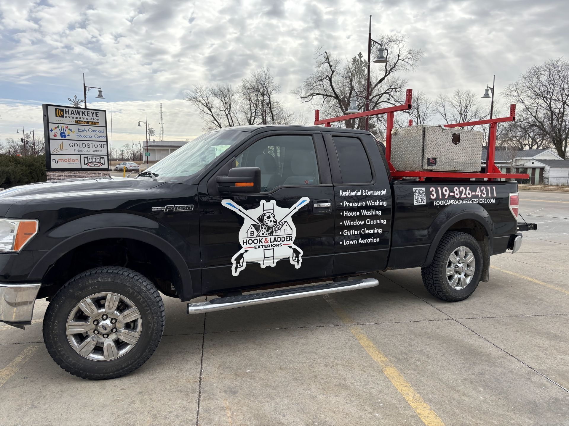 Black pickup truck with red ladder racks parked in a lot, with a skull logo on the door