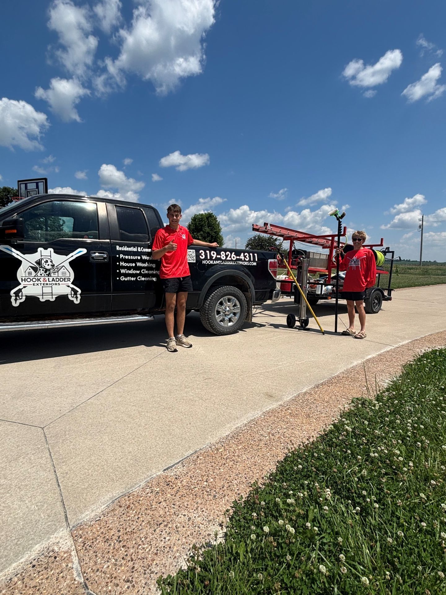 Three people in red shirts stand beside a black tow truck on a sunny roadside under a blue sky.