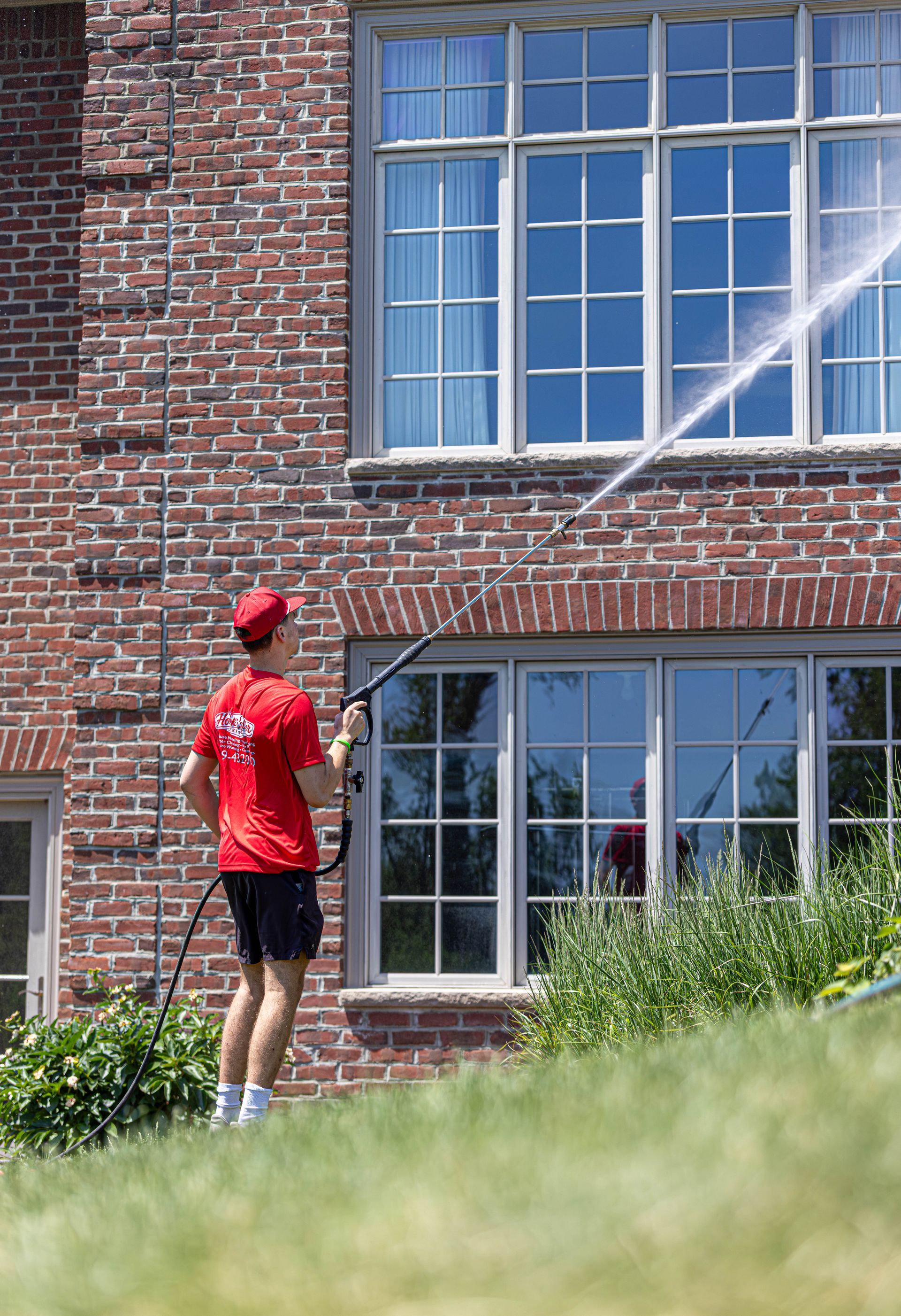 Person in red shirt using a hose to spray water on a brick house window