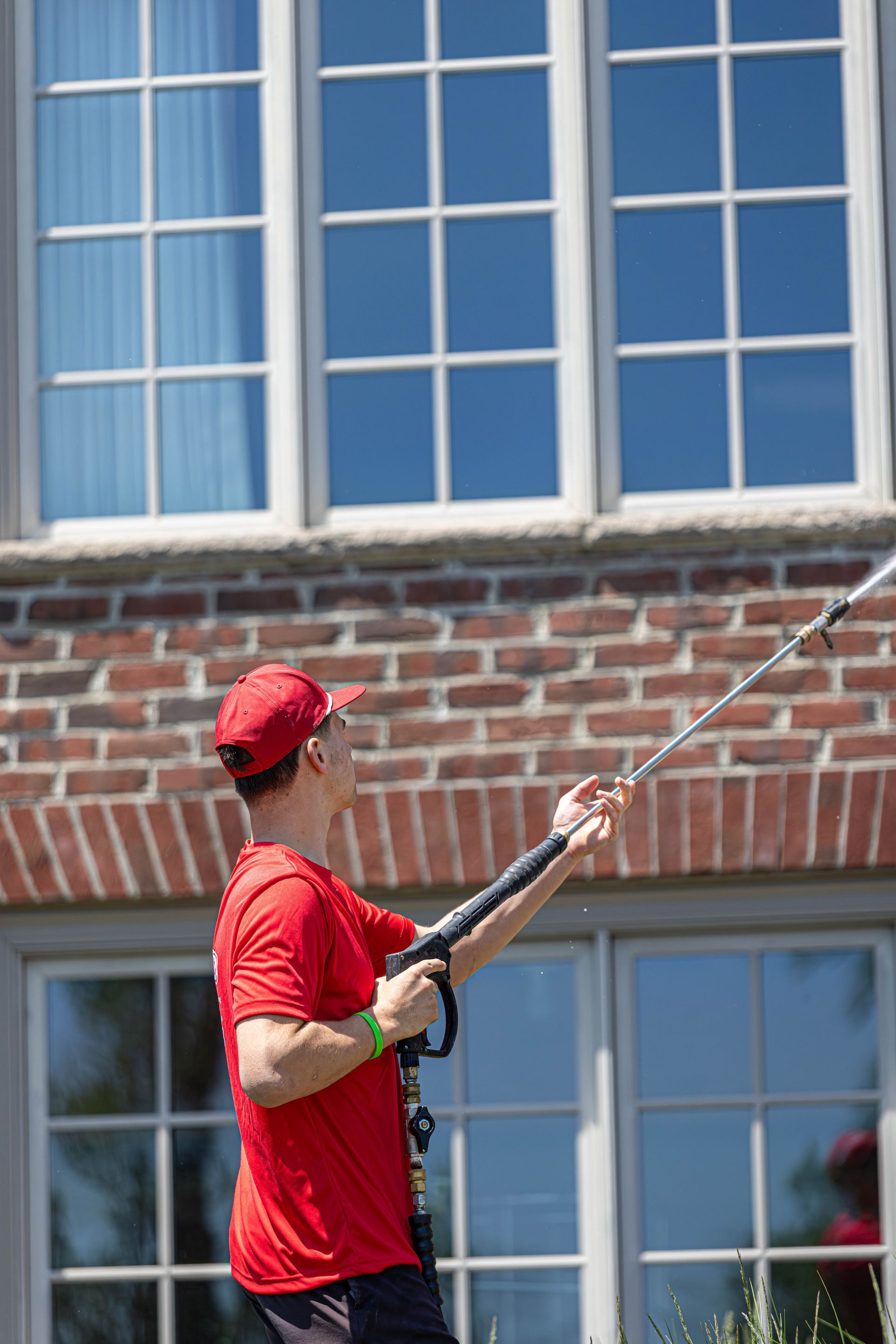 Worker in red shirt using a long pole to clean windows on a brick building