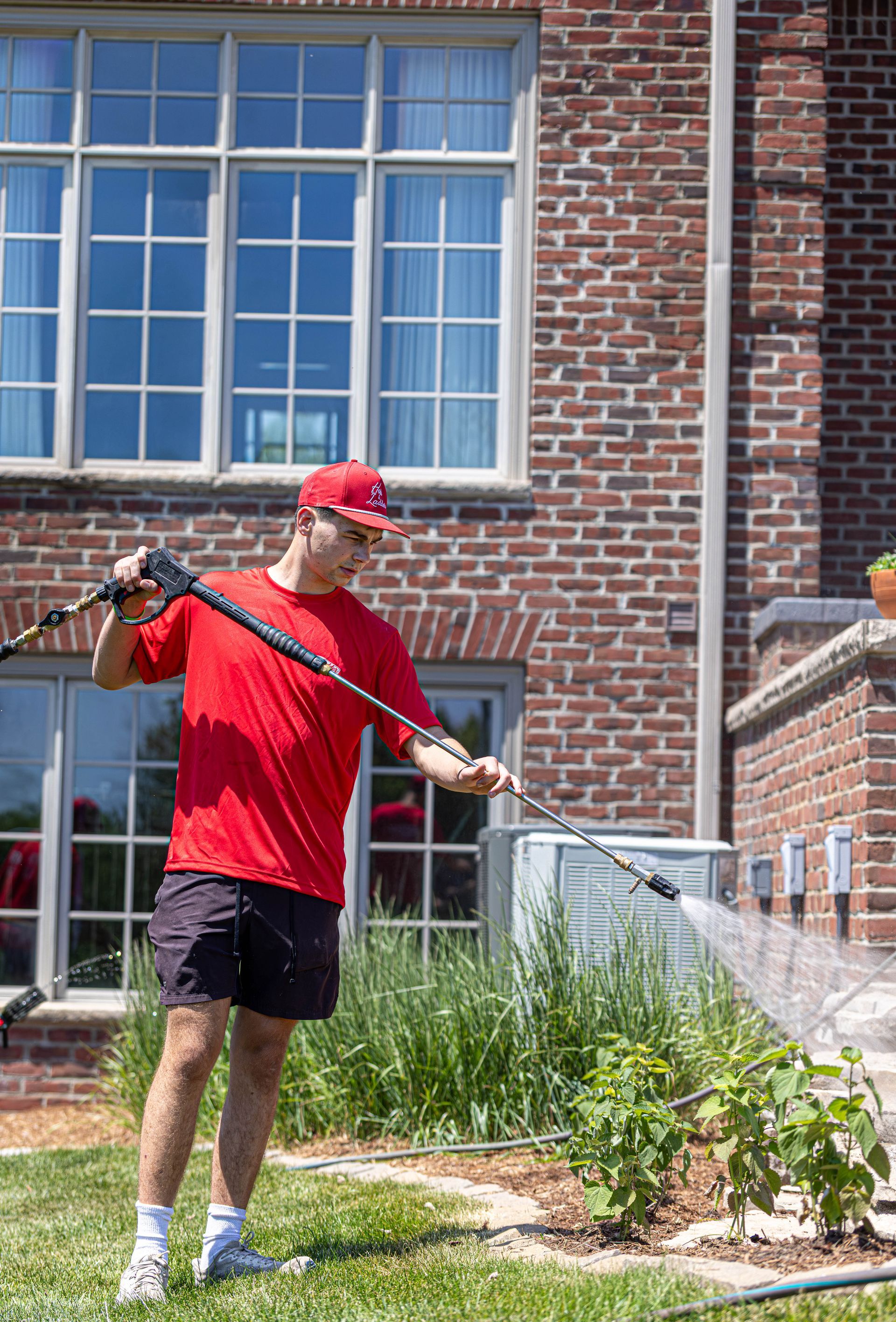 Person in red shirt using a long tool in front of a brick building and window