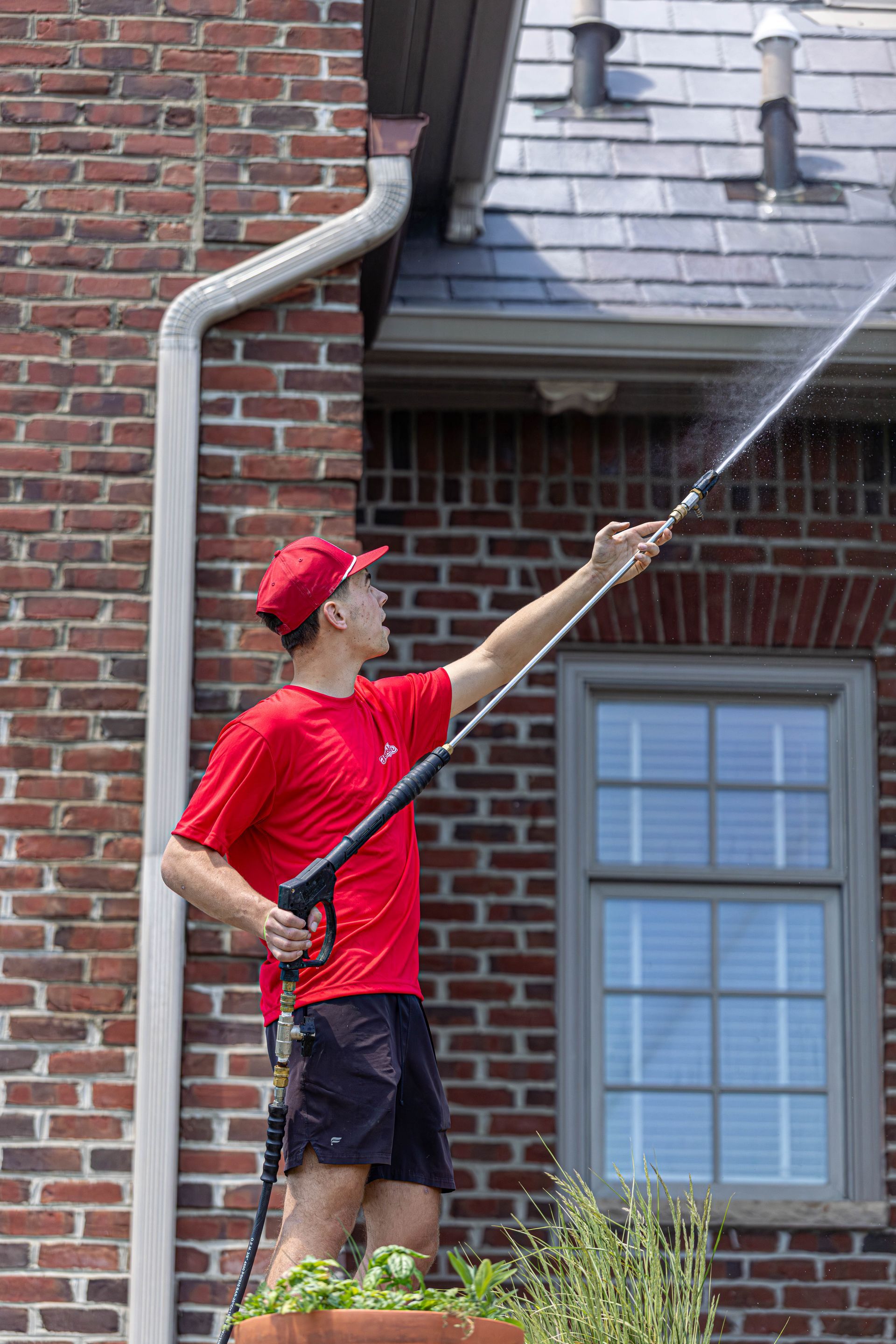 Man in red shirt and cap spraying a house exterior with a pressure washer