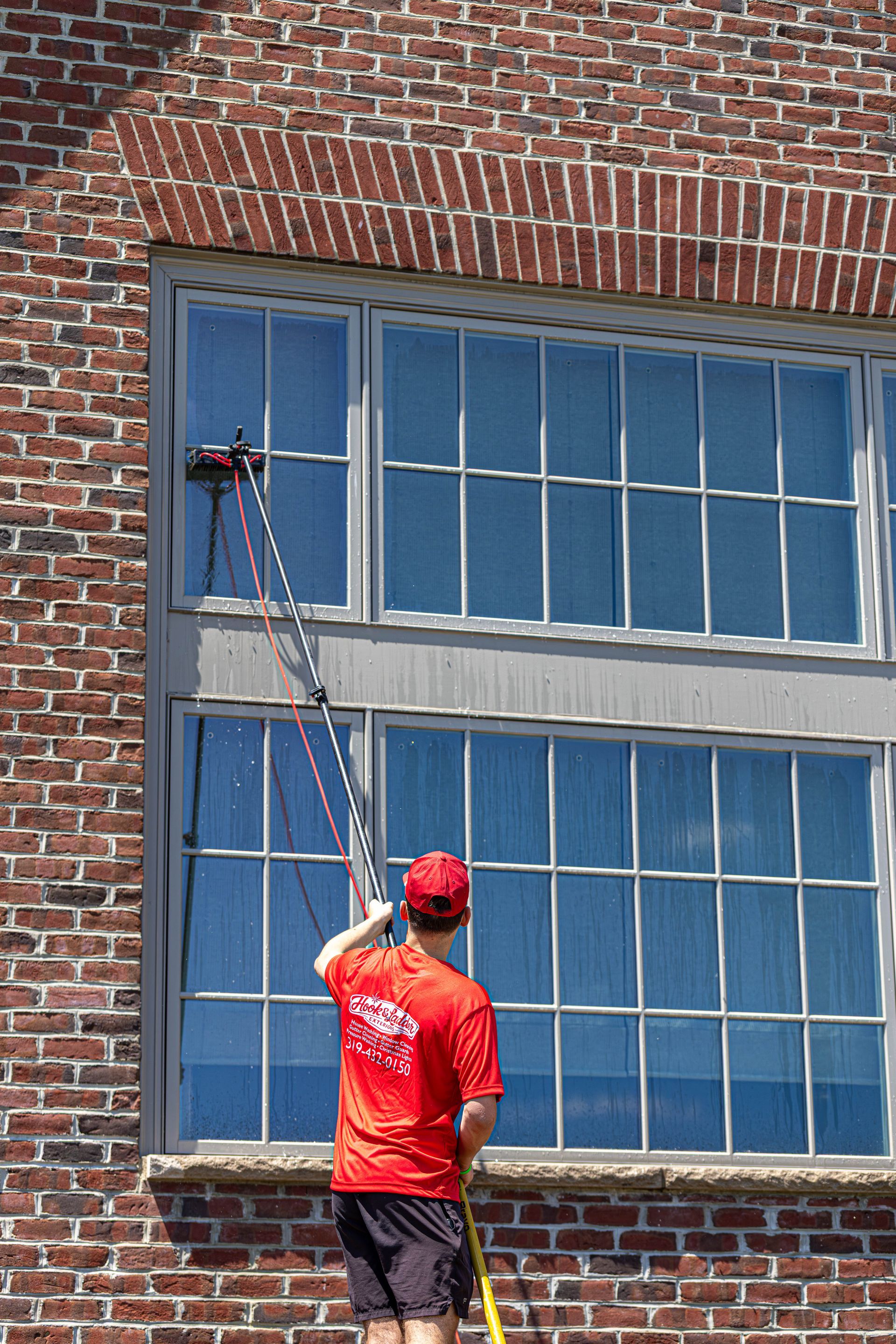 Worker in red shirt cleaning a large brick building window with a rope rig
