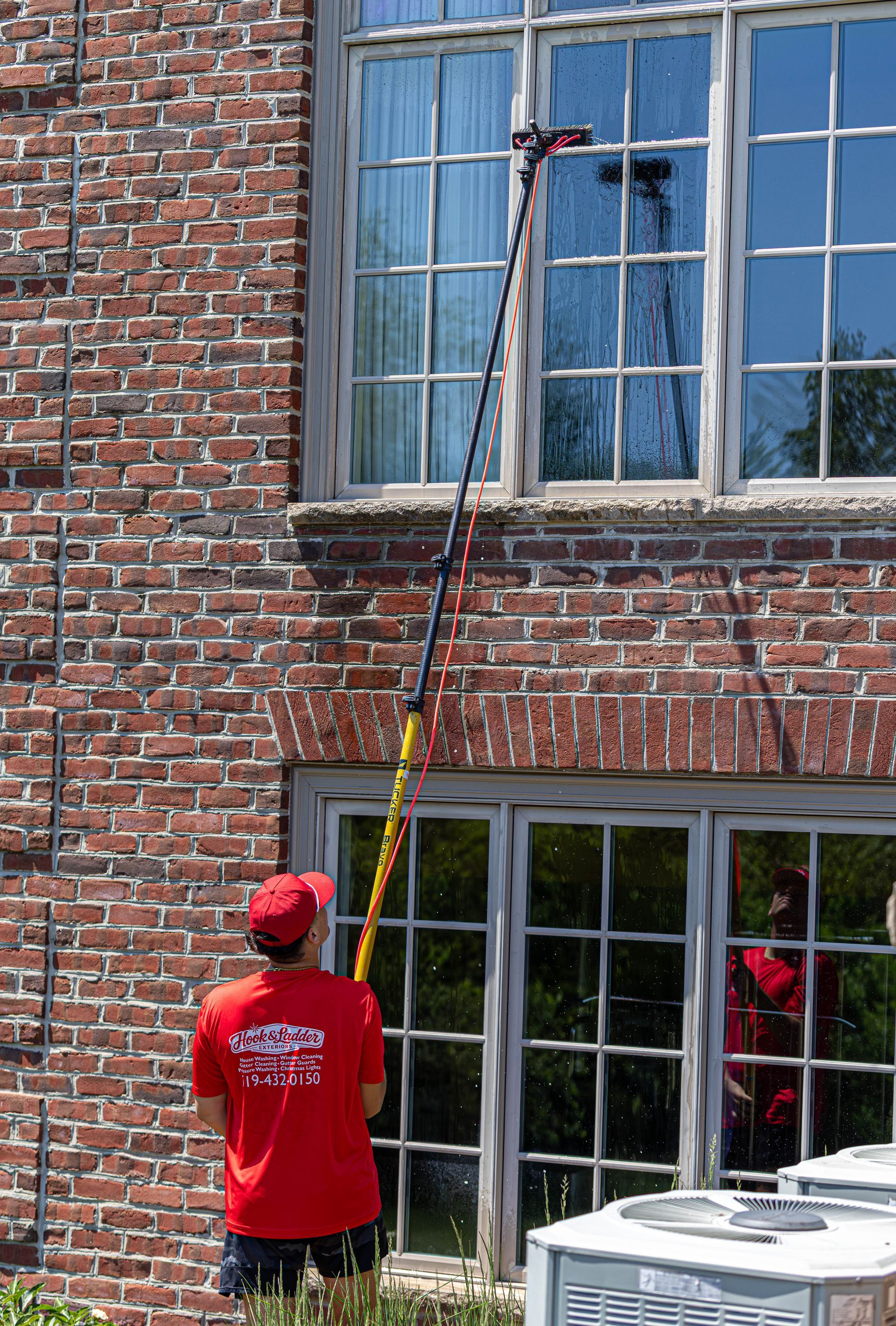 Person using a long pole to clean or inspect a second-story brick building window.