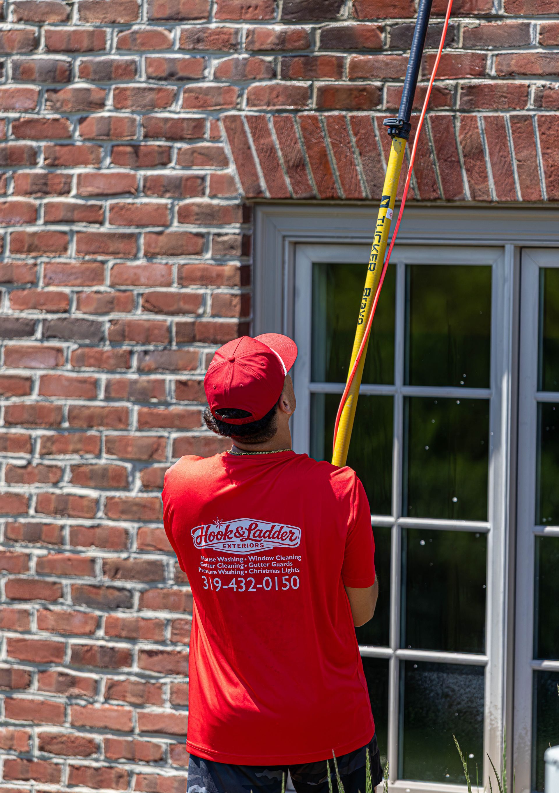 Worker in red shirt using a long pole to clean or paint a brick building above a window