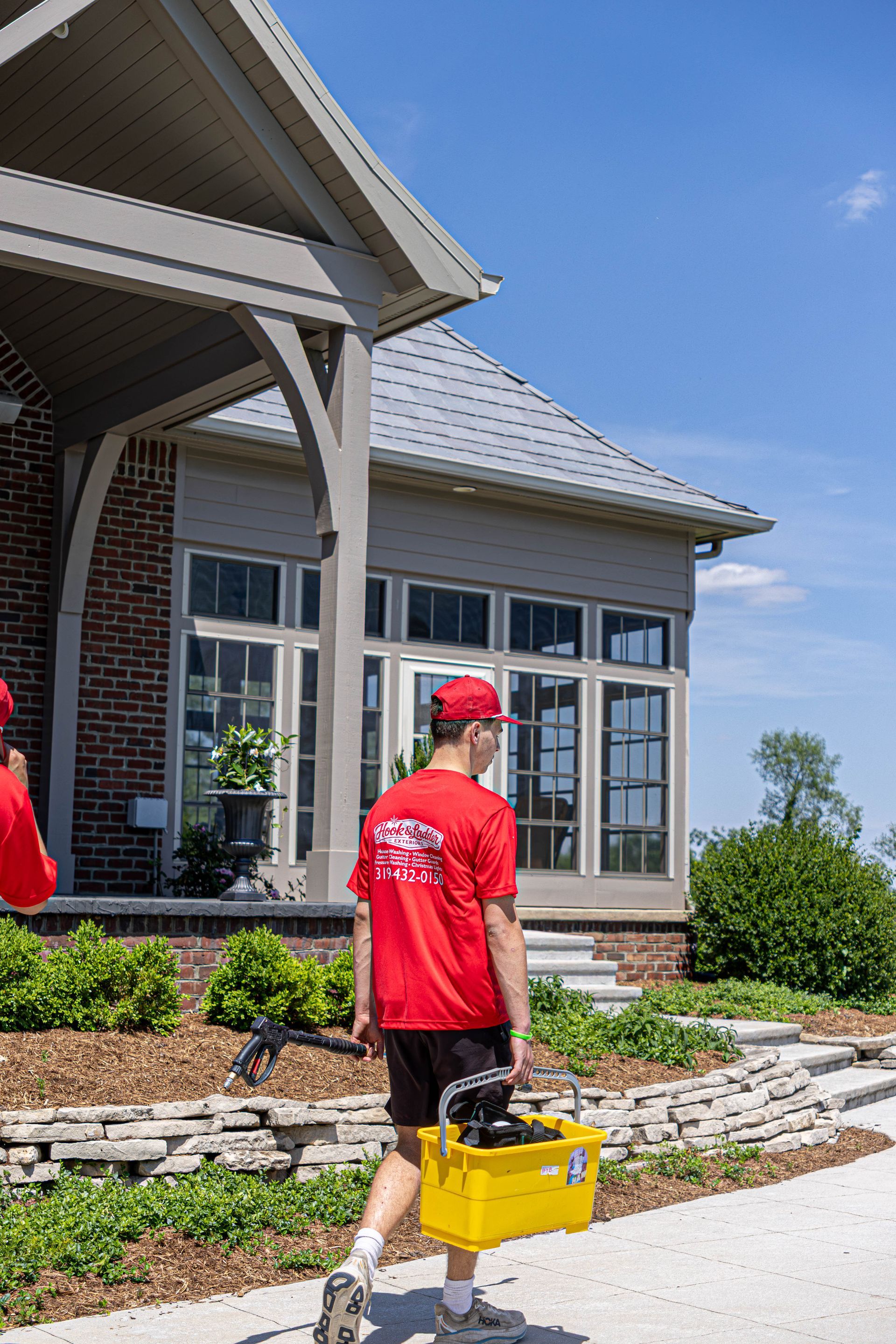 Worker in red shirt carrying a yellow toolbox outside a house under construction