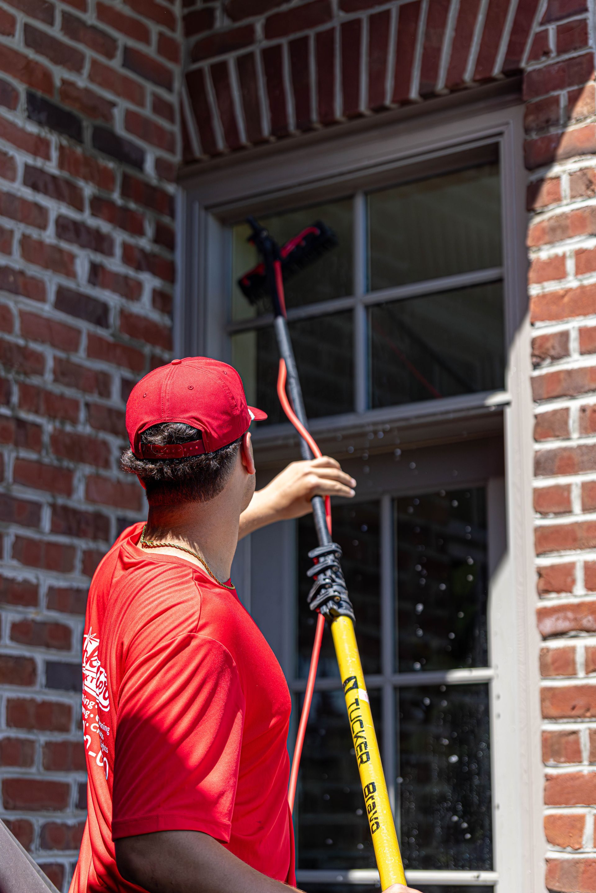 Person in red shirt using a pole tool to inspect a window on a brick building