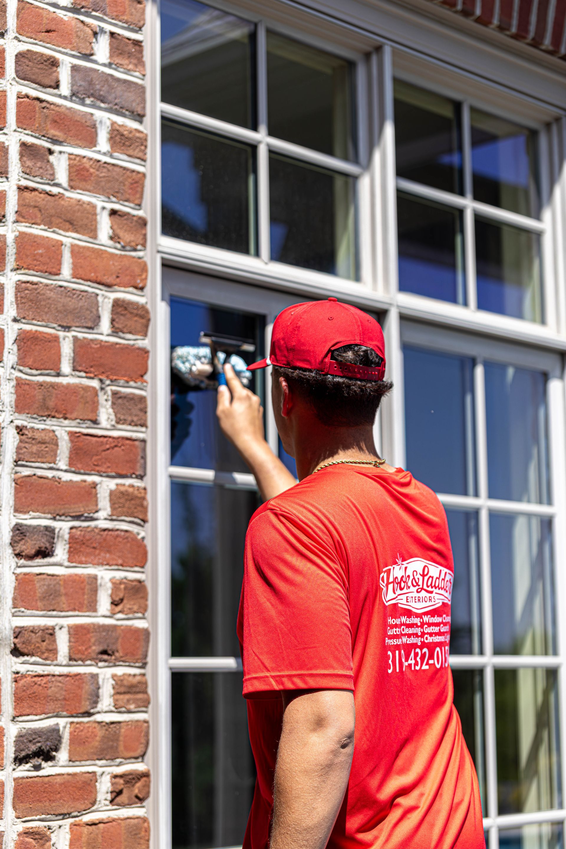 Worker in red shirt and cap painting a brick building window frame with a brush