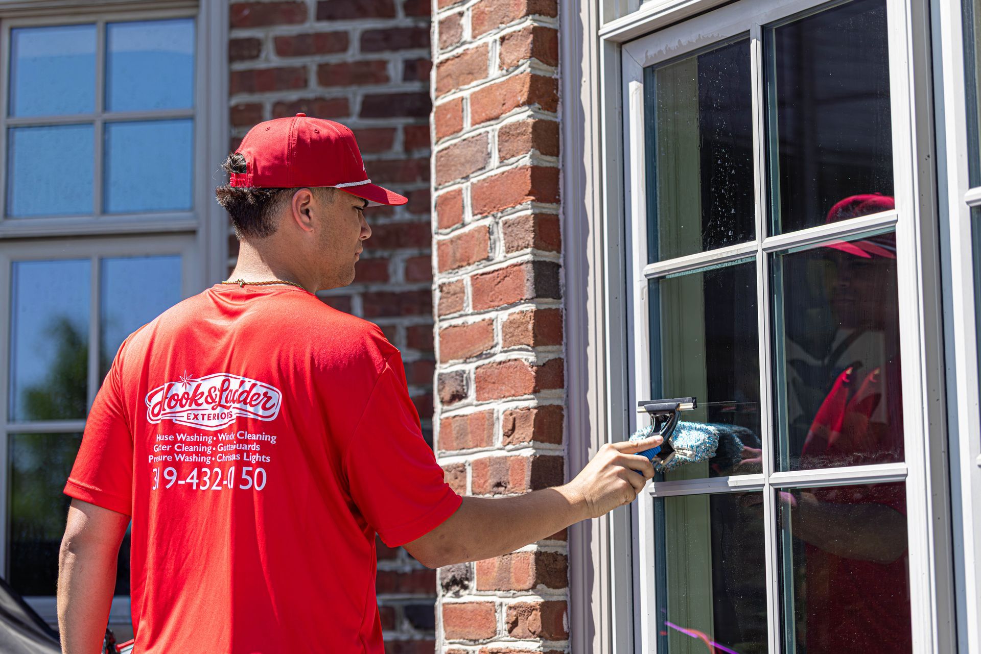 Person in red shirt and cap washing a window on a brick house