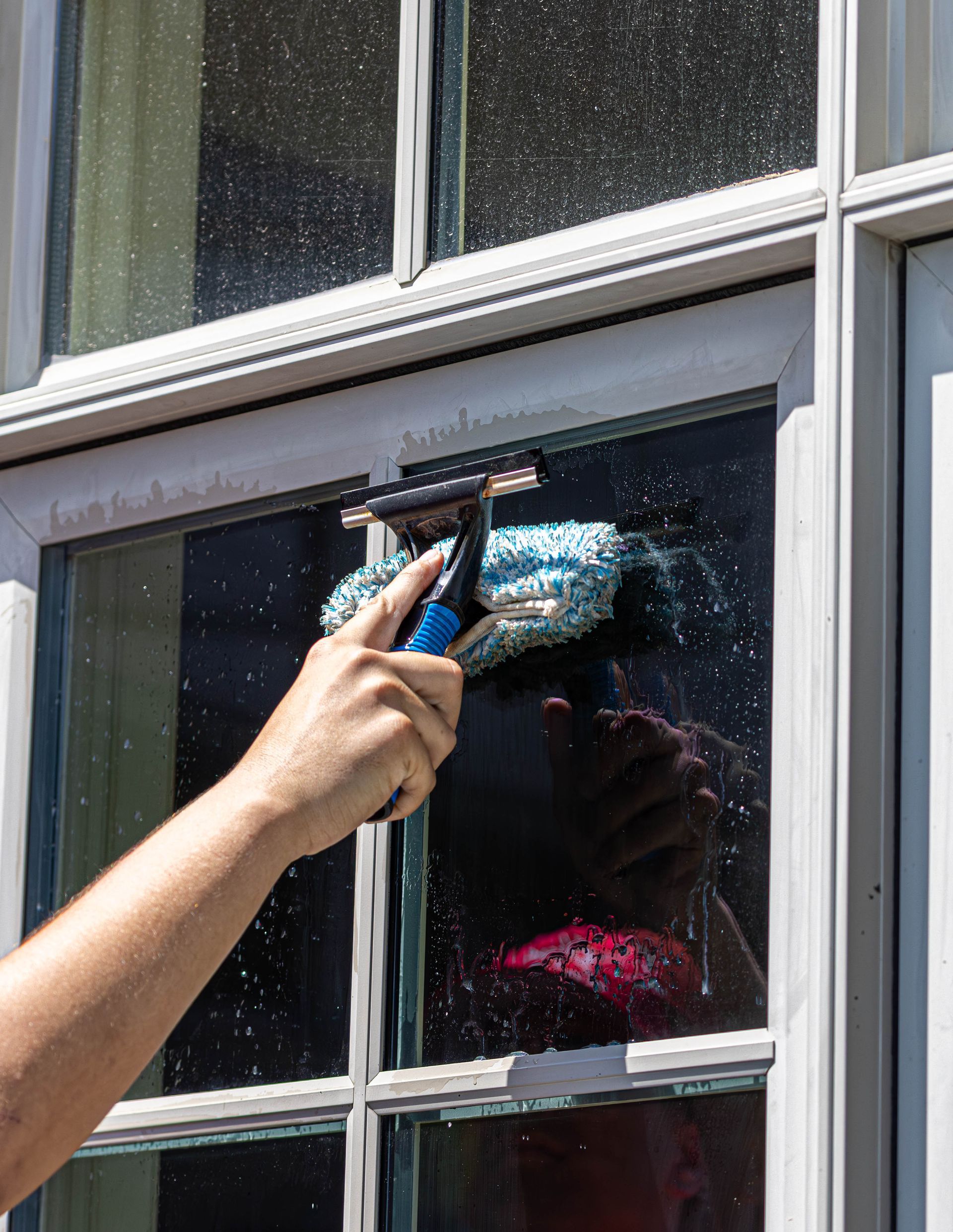 Hand cleaning a window with a blue squeegee, water droplets visible on the glass.