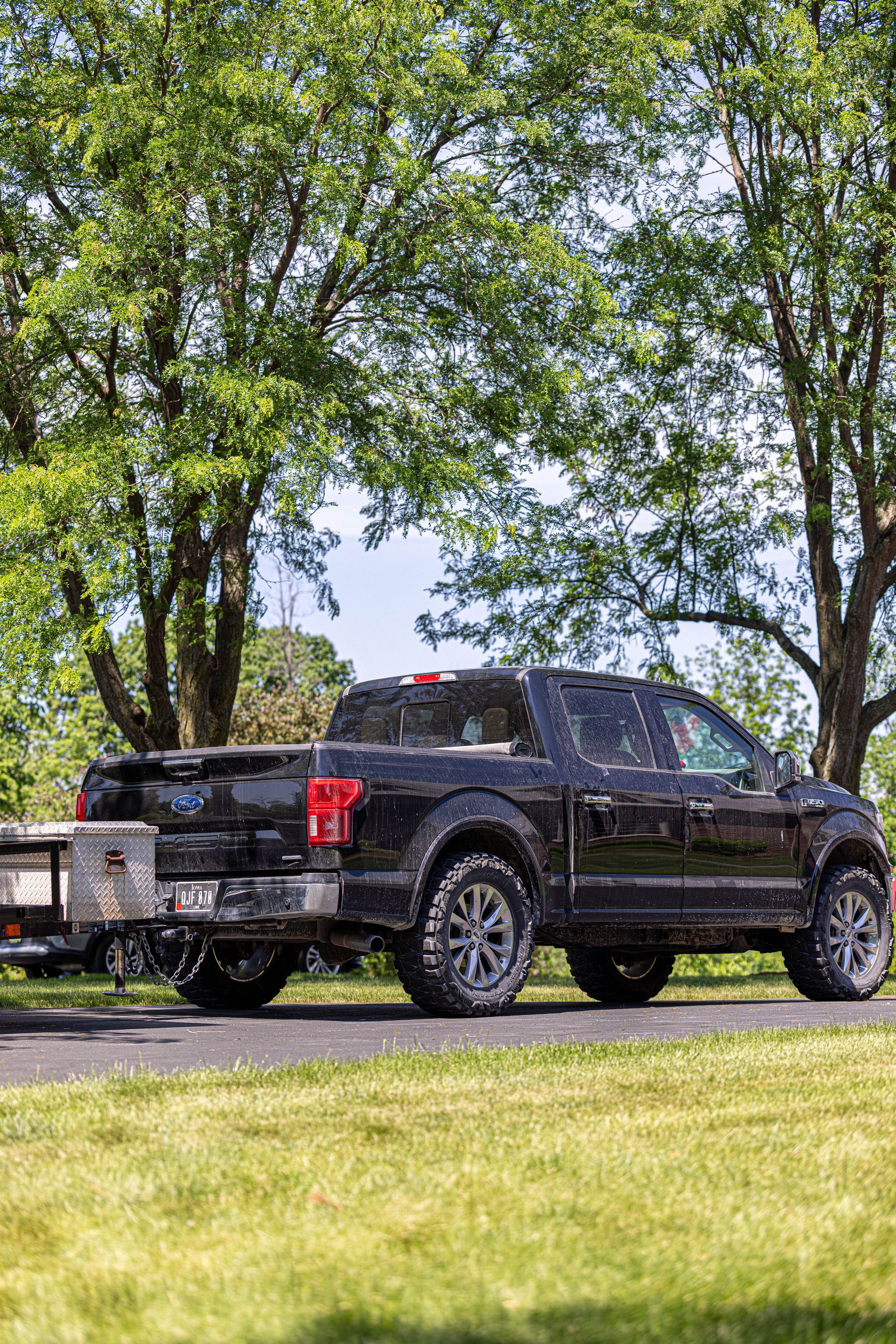 Black pickup truck parked by a road with trees and grass in the background.