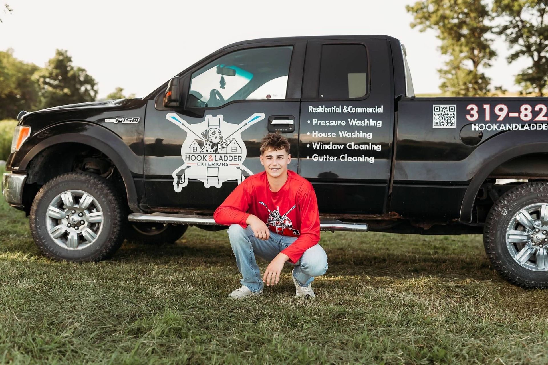 Person crouching in front of a black pickup truck with a business logo and contact information on the side