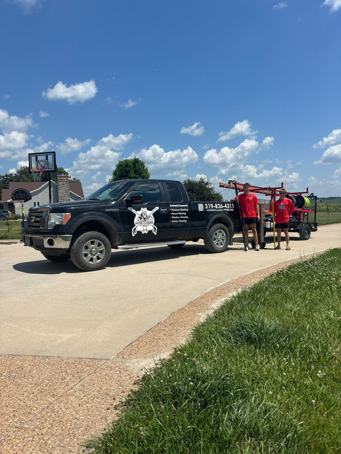 Black pickup truck with logo parked on a road; four people in red shirts stand beside it under a blue sky.