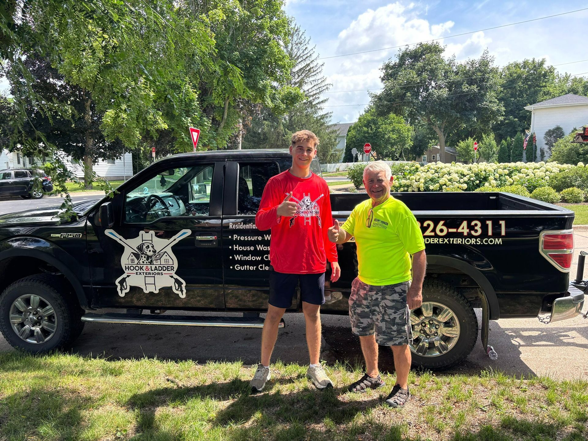 Two people standing beside a black pickup truck in a sunny outdoor lot with trees and bushes.