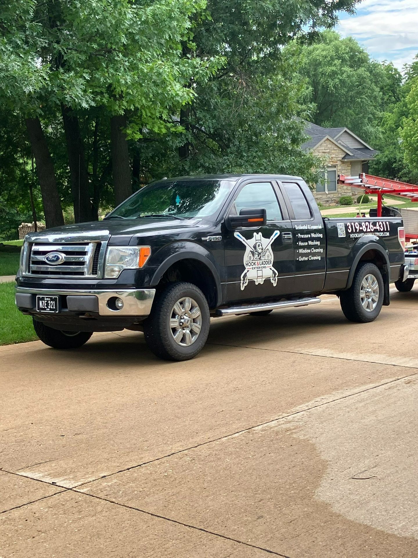 Black pickup truck with white decals parked on a wet street beside trees and a house