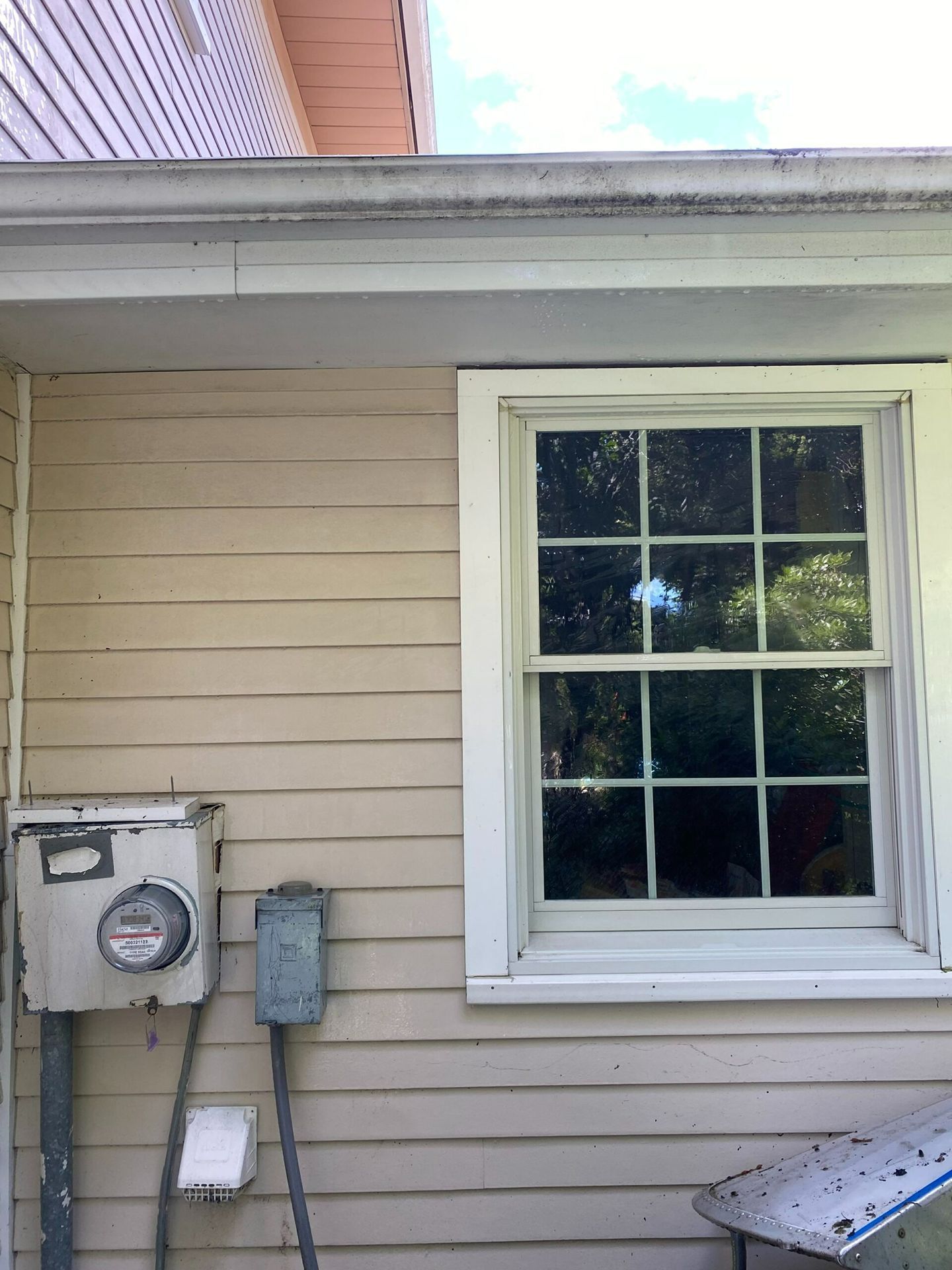 House exterior with beige siding, a window, utility meters, and a roof overhang with a gutter.