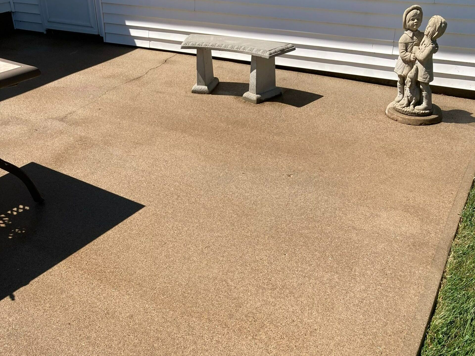 Outdoor patio with tan concrete, a small bench, and a decorative stone statue by a white house wall