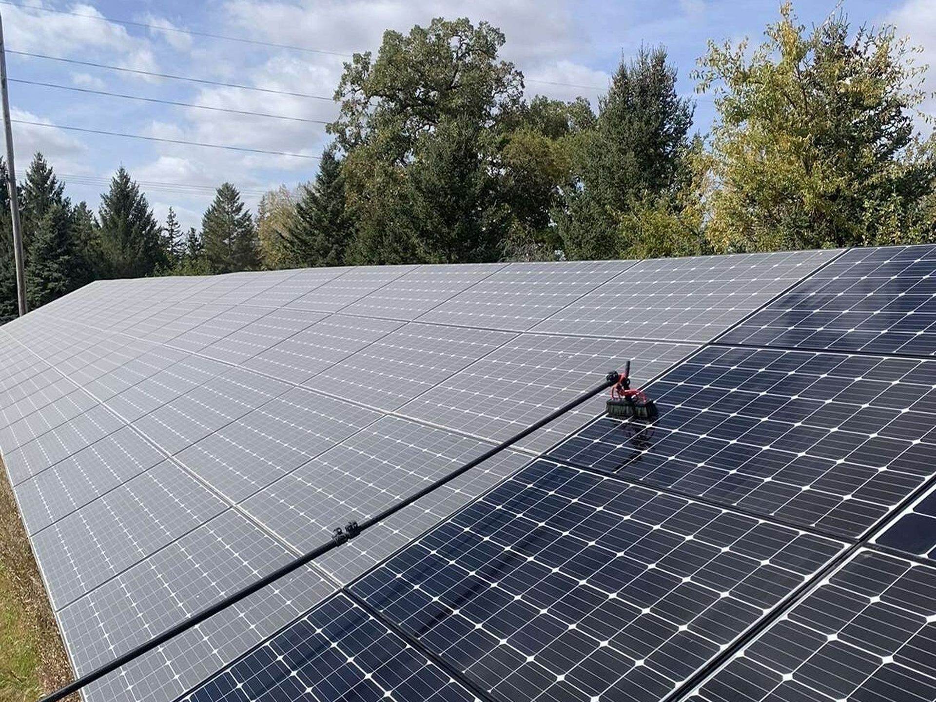 Solar panels covering a hillside, with a worker using a red tool to inspect them under a cloudy sky