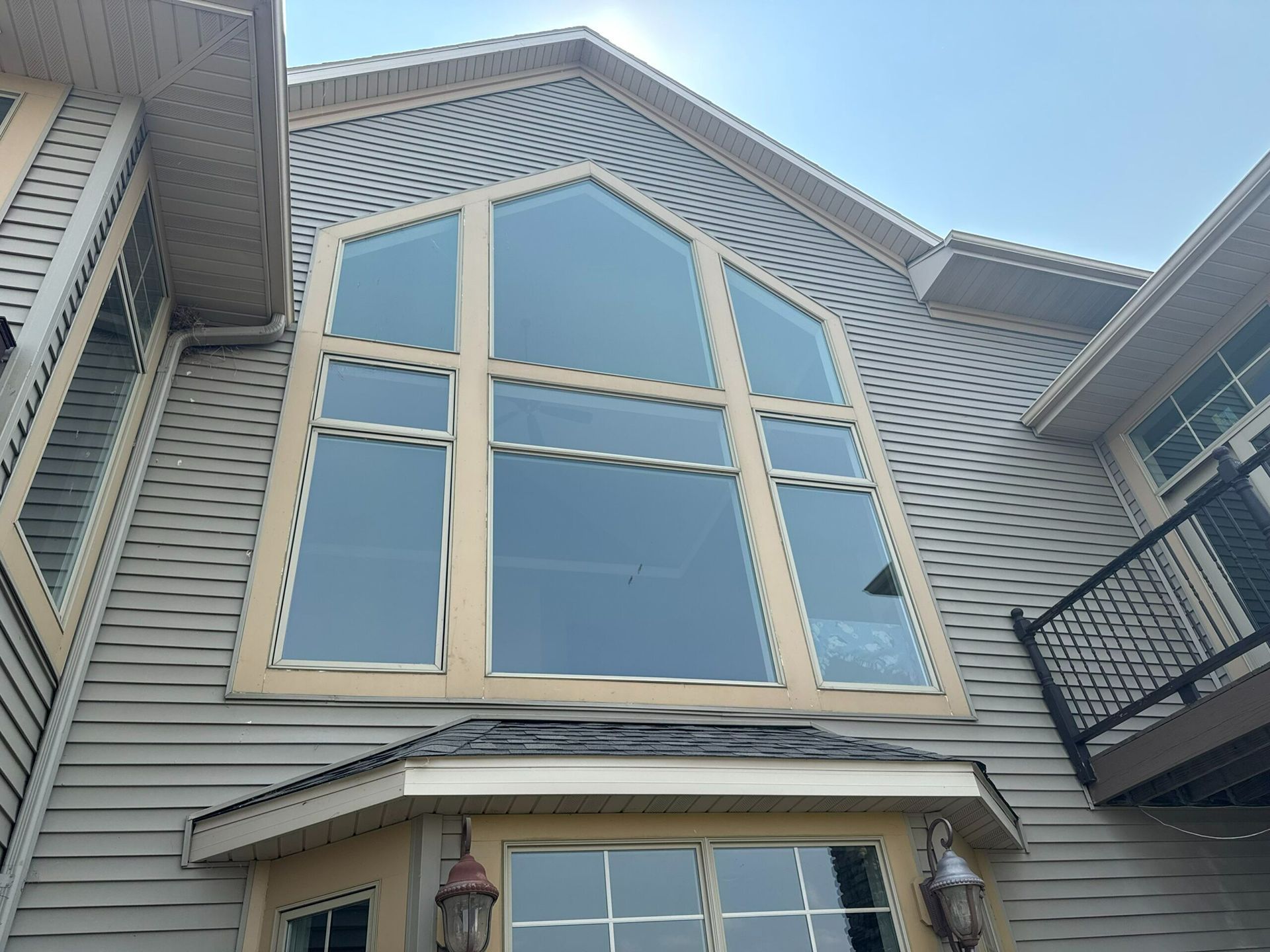 Gray house exterior with a large arched window and balcony on the right.