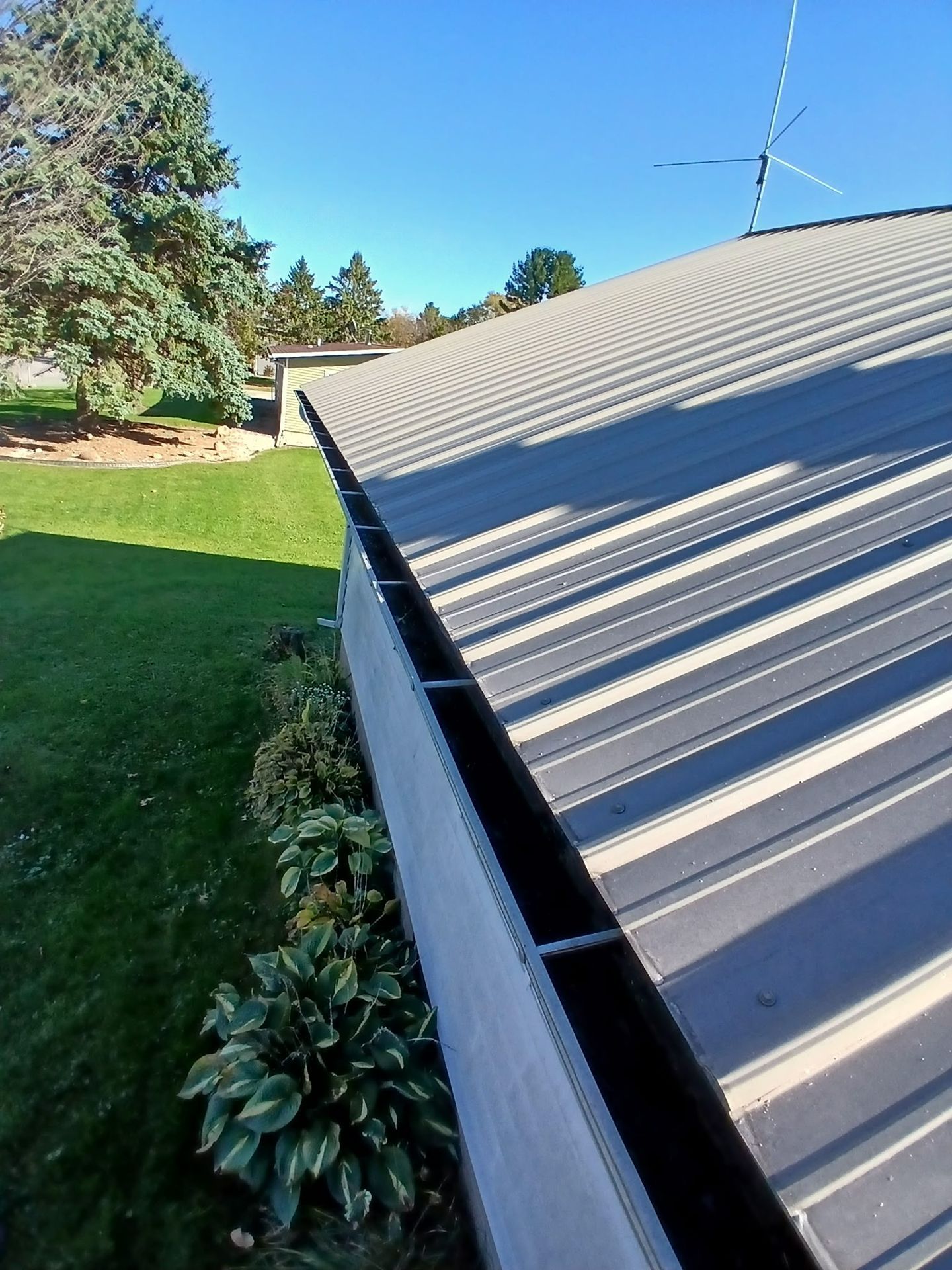 Corrugated metal roof beside a green lawn and trees on a sunny day