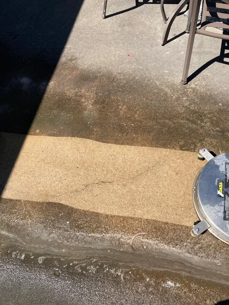 Wet concrete patio with a dark shadow, tan surface, and a round table leg at the edge