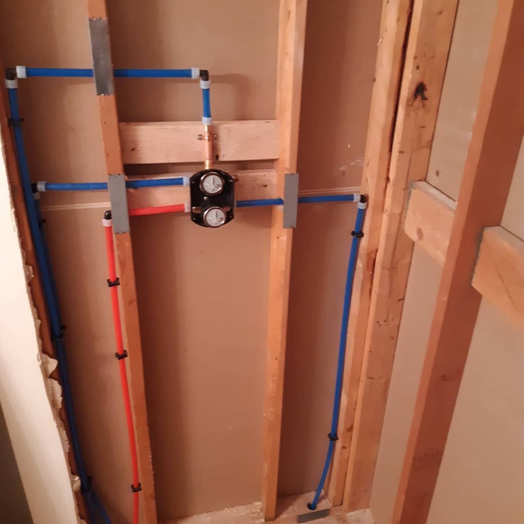 Pipes and a shower valve installed in a wall during construction. Blue and red pipes are visible.
