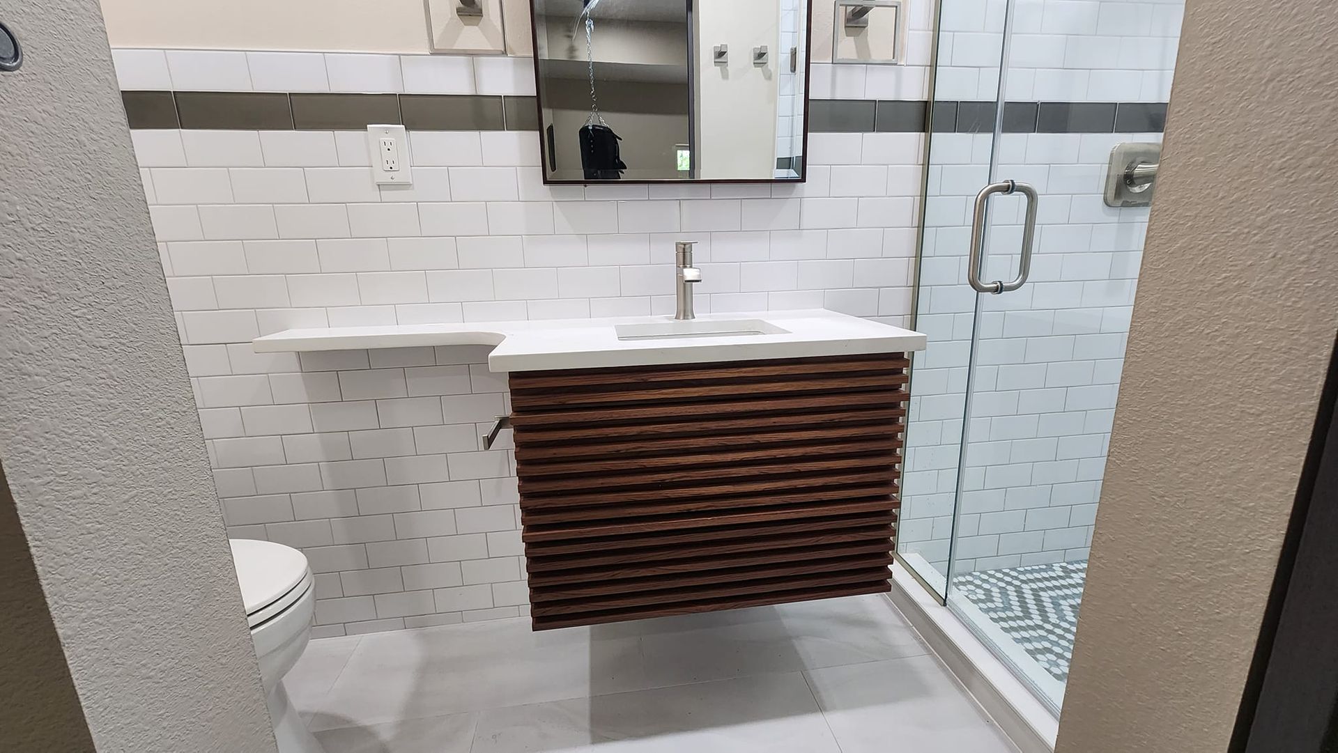 Bathroom with white tiled walls, wooden vanity, and glass shower.