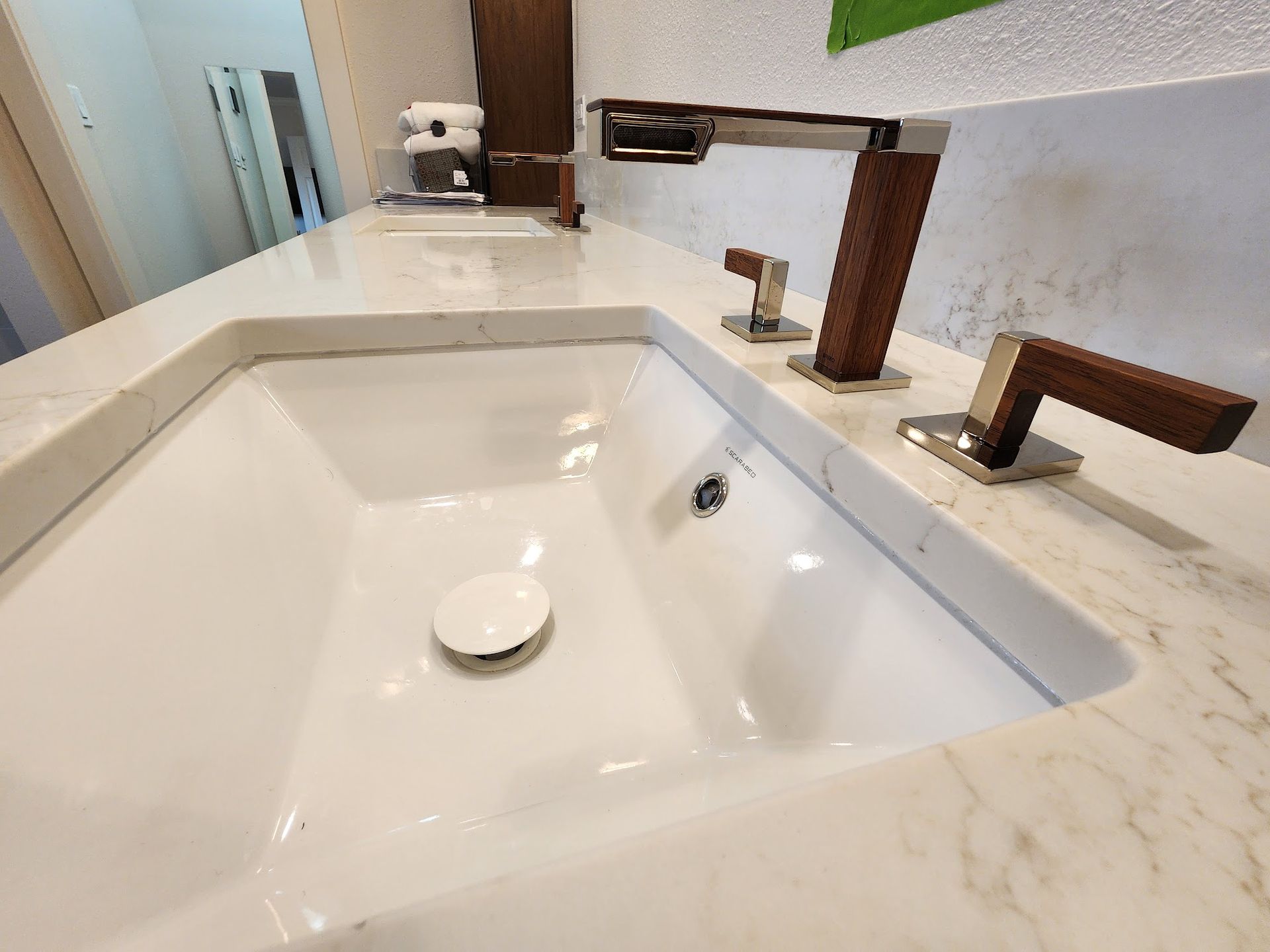 White bathroom sink with marble countertop and wood-accented faucet and handles.