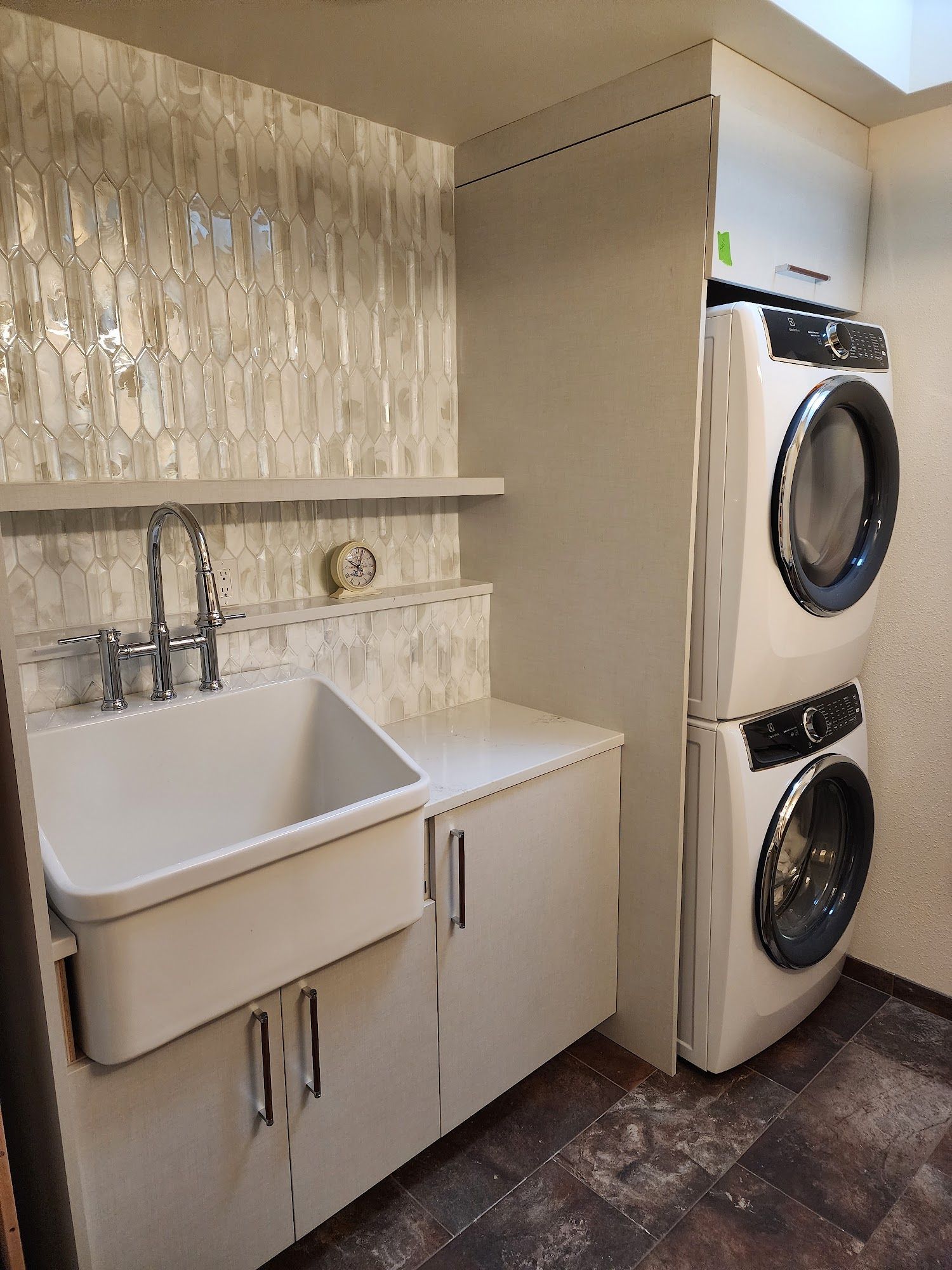 Laundry room with stacked washer/dryer, sink with backsplash, and cabinets.