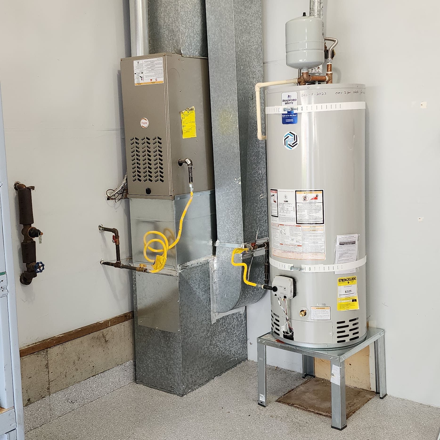 A furnace and water heater are in a utility room. The water heater is on a metal stand.
