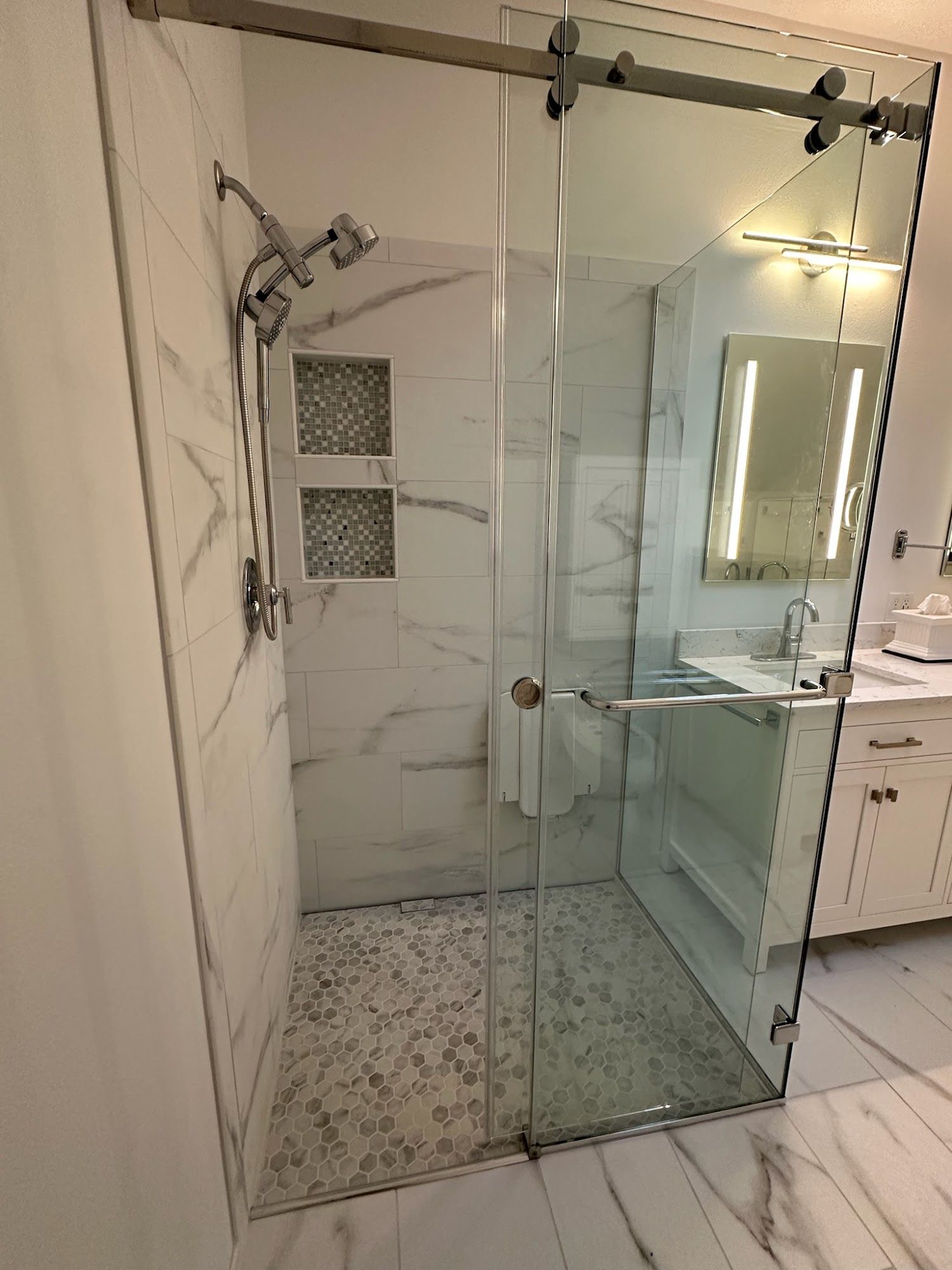 Glass shower with marble walls, mosaic floor, and sliding door. Modern bathroom with vanity visible.