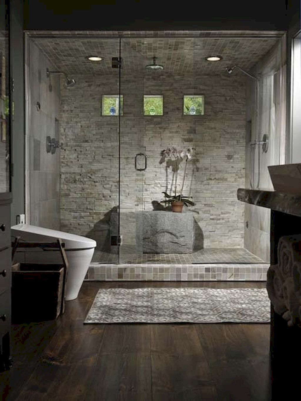 Luxurious bathroom with stone shower, glass door, and orchid on a rock.