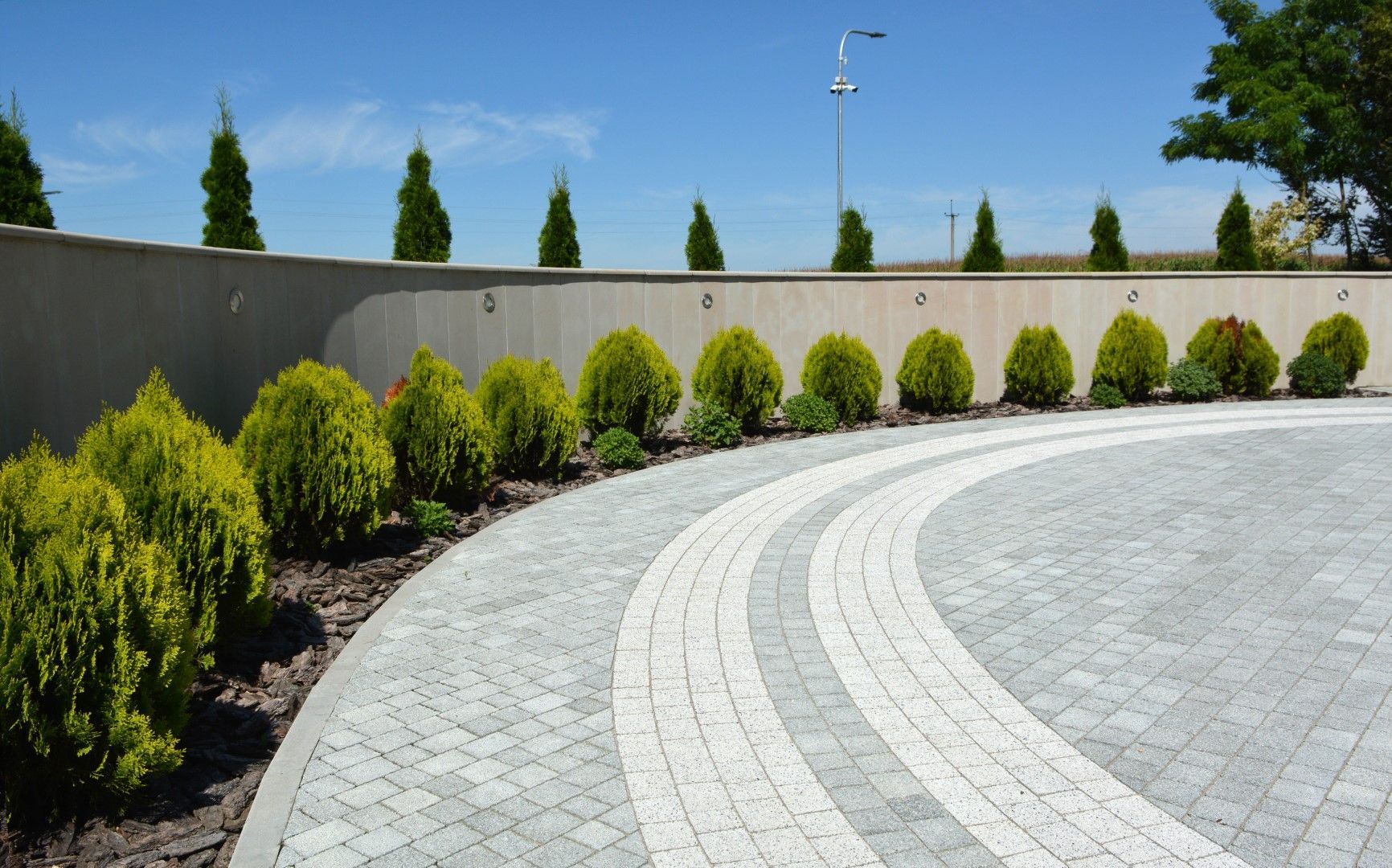 A curved driveway with a row of bushes on the side of it.